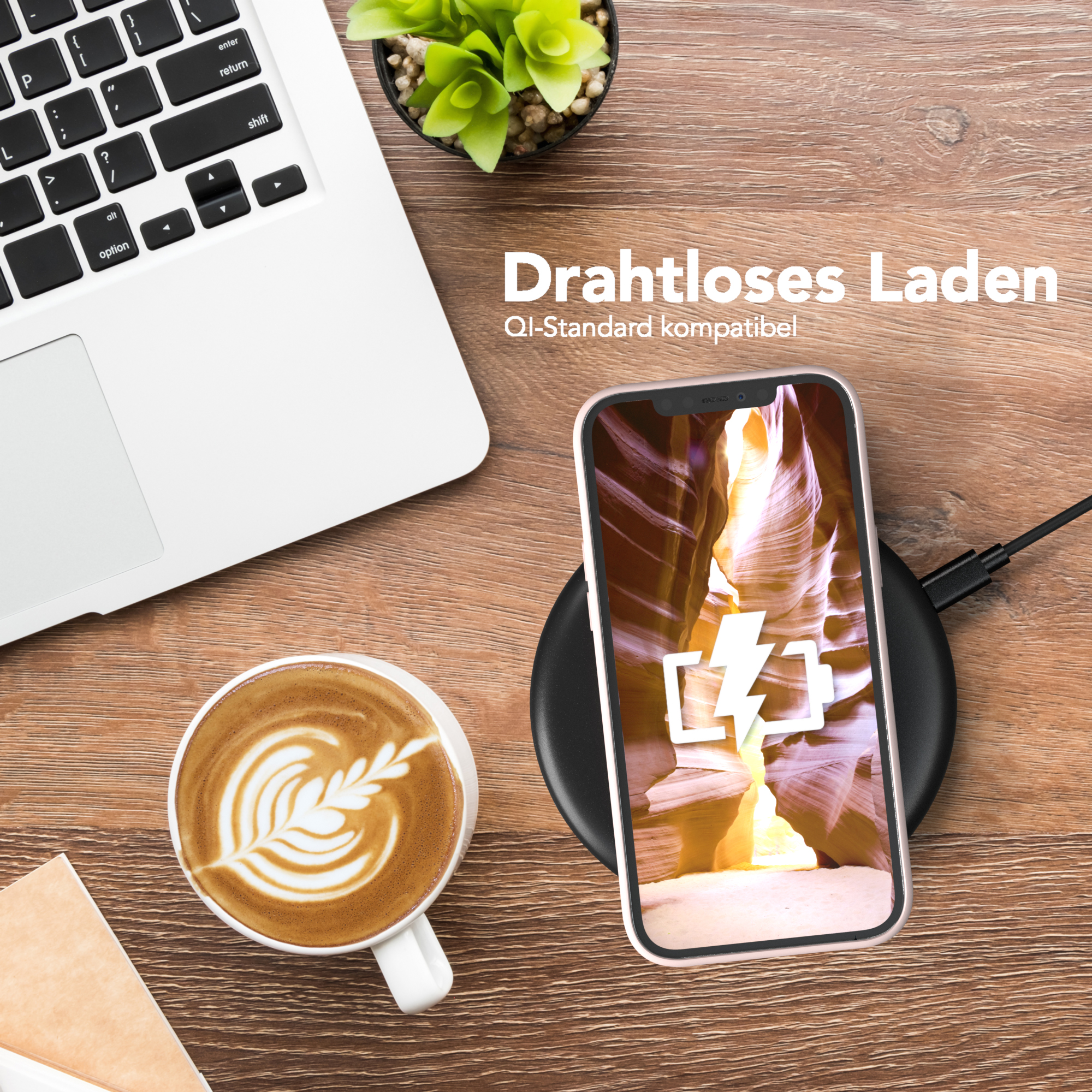 Laptop, Kaffee, Telefon lädt auf Pad. Das Telefon zeigt ein Canyon-Bild. Holzoberfläche.