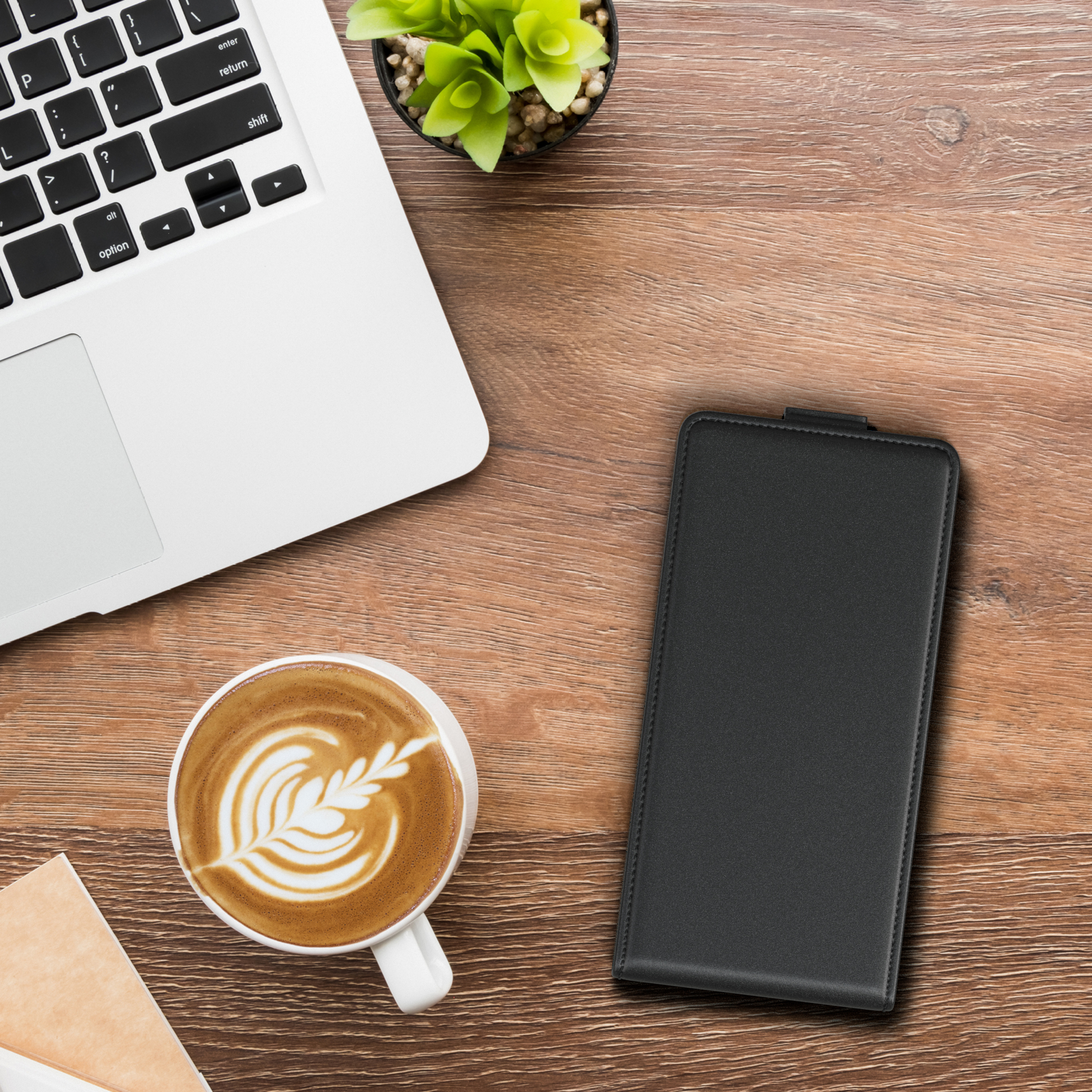 Laptop, Kaffee mit Kunst, Notizblock und schwarze Handyhülle auf einem Holztisch, Draufsicht.