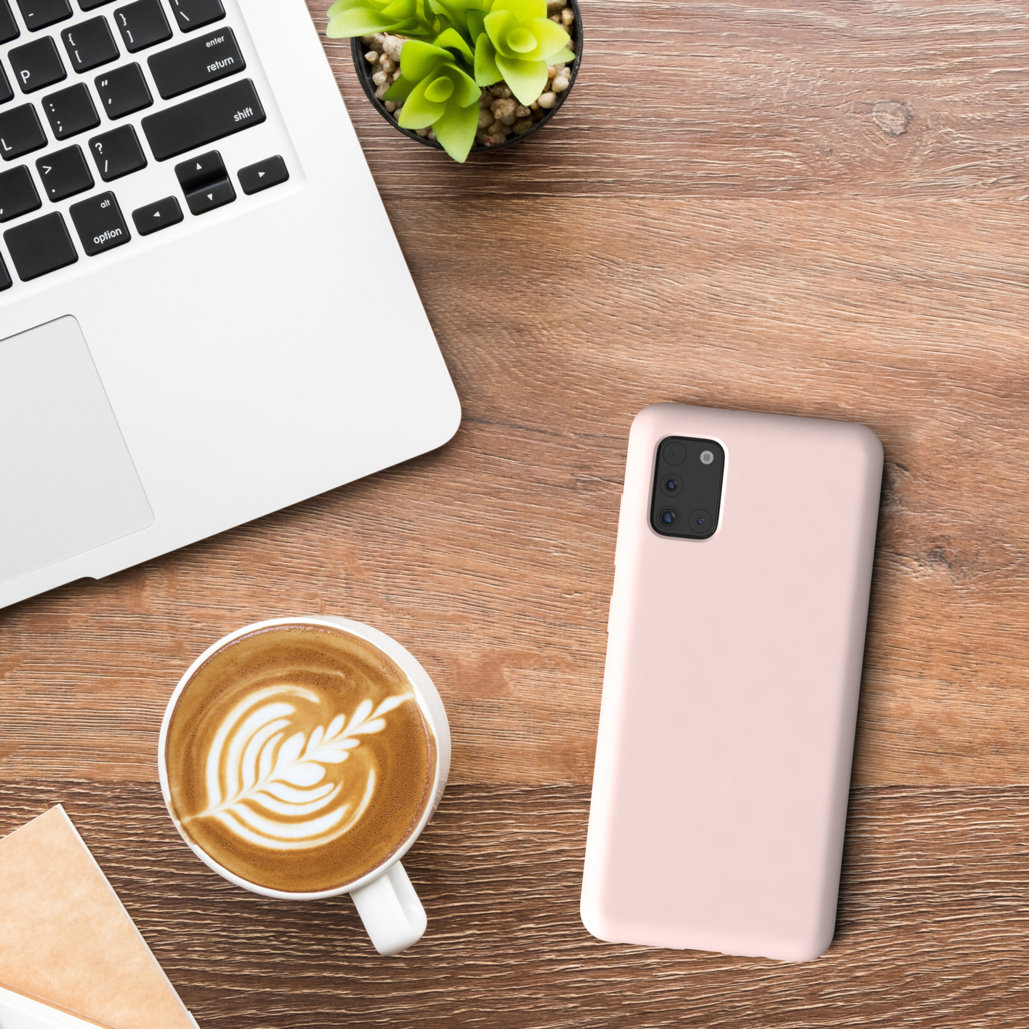 Schreibtisch mit Laptop, Kaffeetasse, kleiner Pflanze und Telefon mit rosa Hülle.
