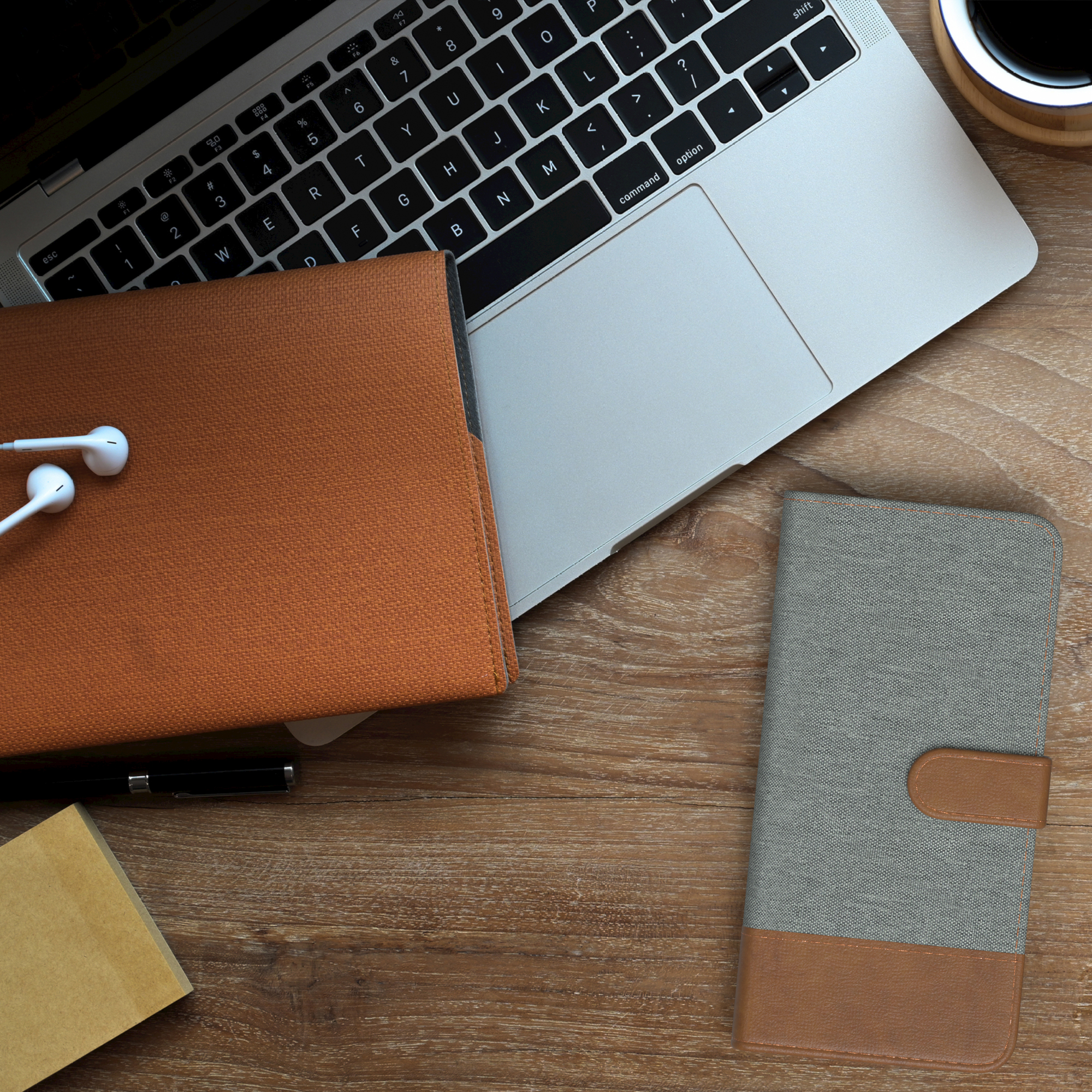 Laptop, Kopfhörer, orangefarbene Hülle und graue Handyhülle auf Holz.
