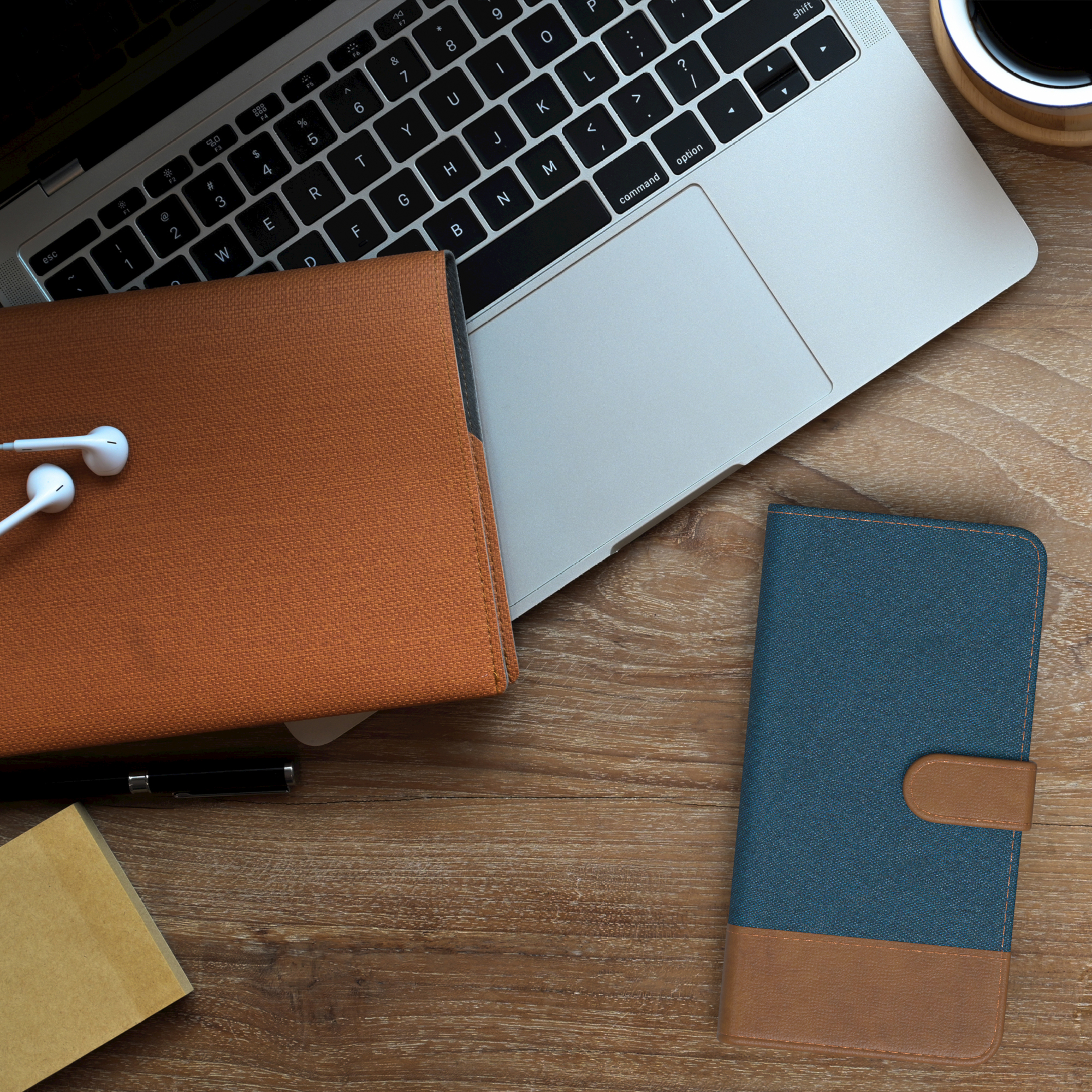 Ein Laptop, ein Notizbuch, ein Stift und eine Handyhülle auf einem Holzschreibtisch.