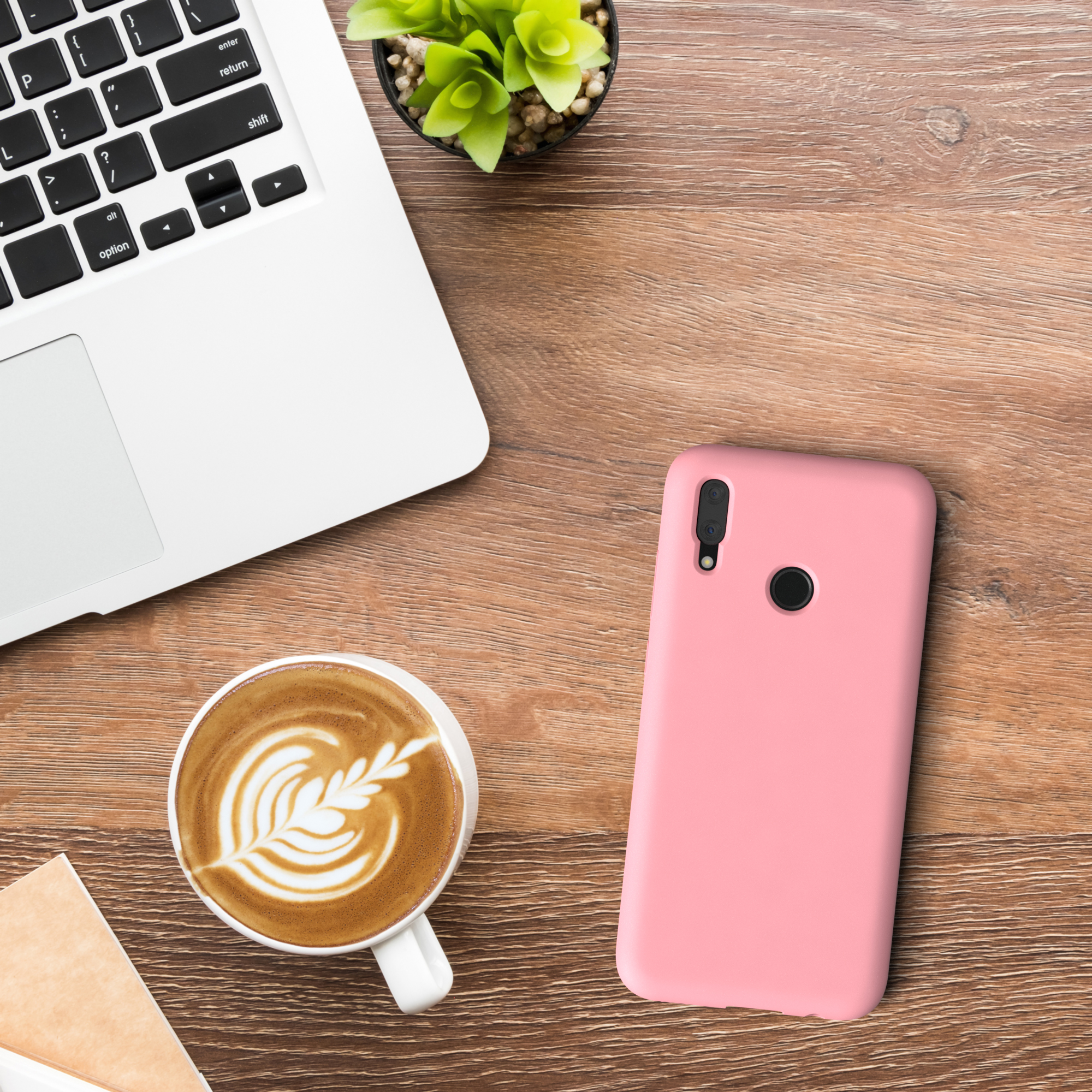 Ein Laptop, Kaffee mit Latte Art, eine rosa Handyhülle und eine Pflanze auf Holztisch.