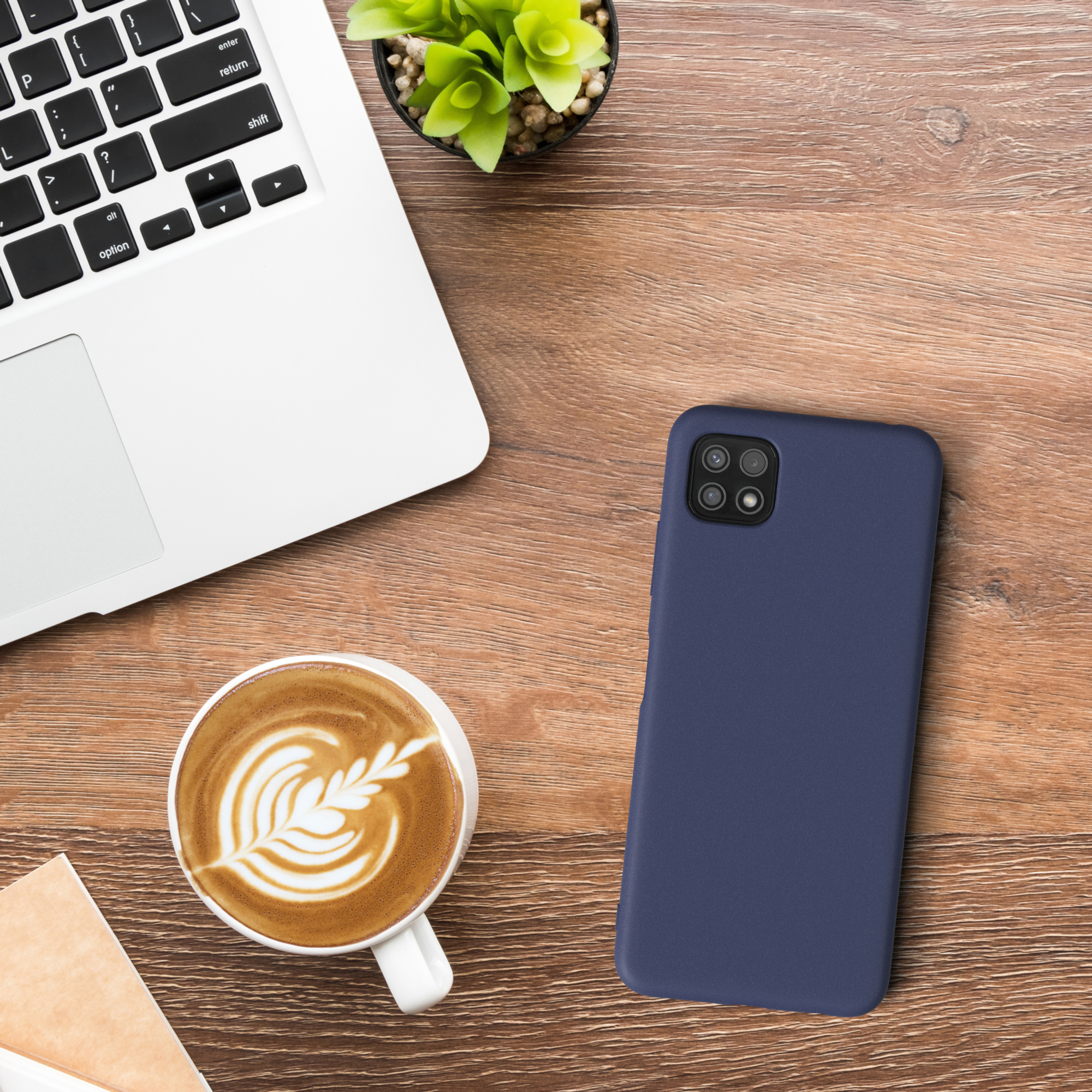 Draufsicht auf einen Schreibtisch mit Laptop, Kaffee, Telefon und Pflanze. Das Telefon ist blau.