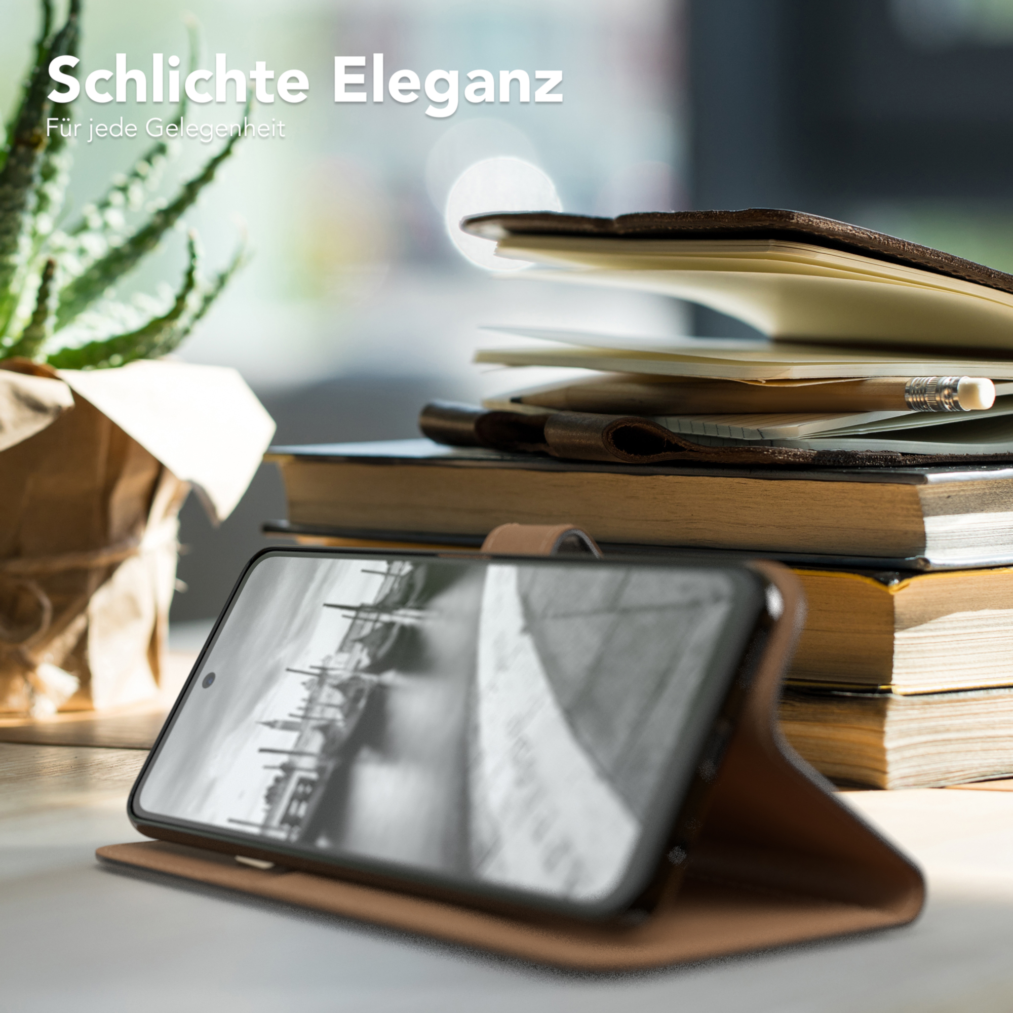 Telefon in brauner Lederhülle auf Holztisch, Bücher und Pflanze im Hintergrund.
