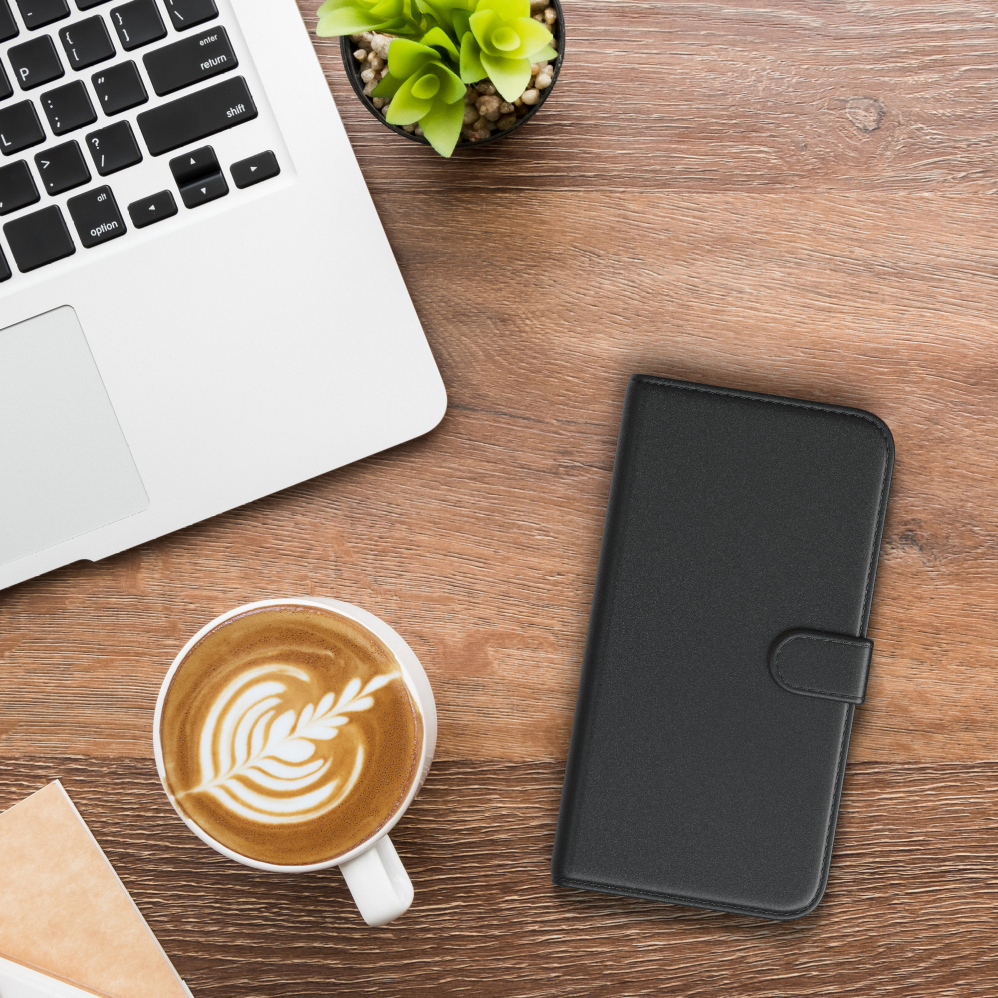 Laptop und Kaffeetasse auf einem Holztisch, Handyhülle in der Nähe.