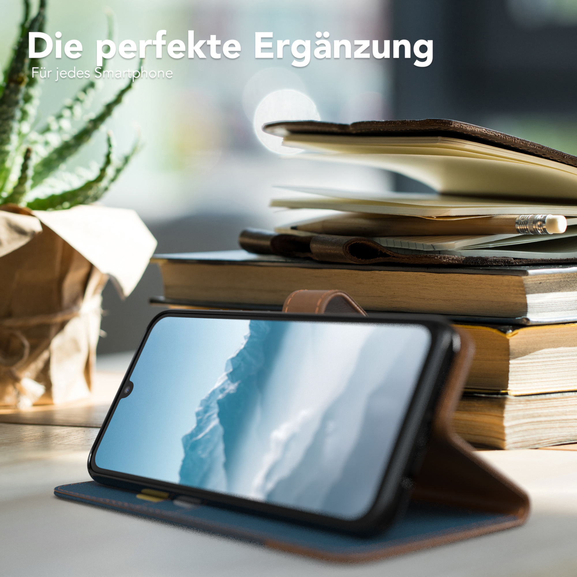 Telefon in Hülle auf Schreibtisch mit Büchern und Pflanze. Zeigt ein Bild.