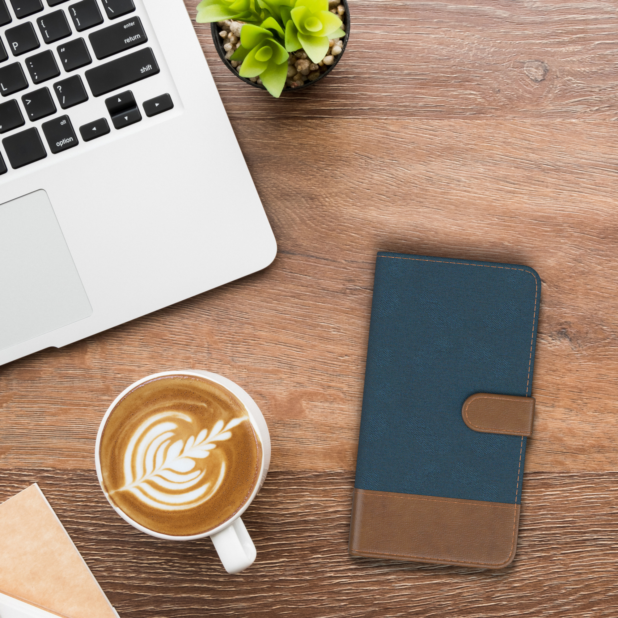 Laptop, Kaffee mit Kunst und Handyhülle auf einem Holztisch.