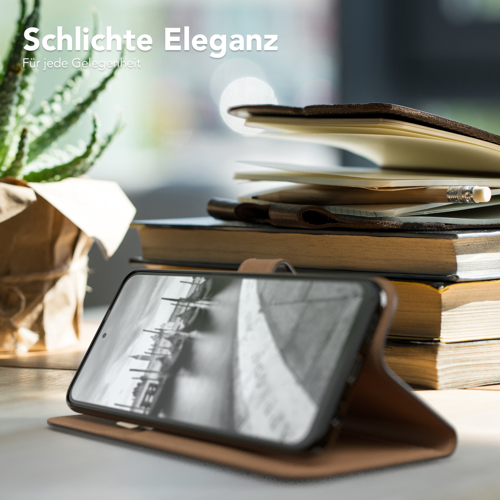 Telefon in brauner Hülle auf einem Schreibtisch, mit Büchern und Pflanze.