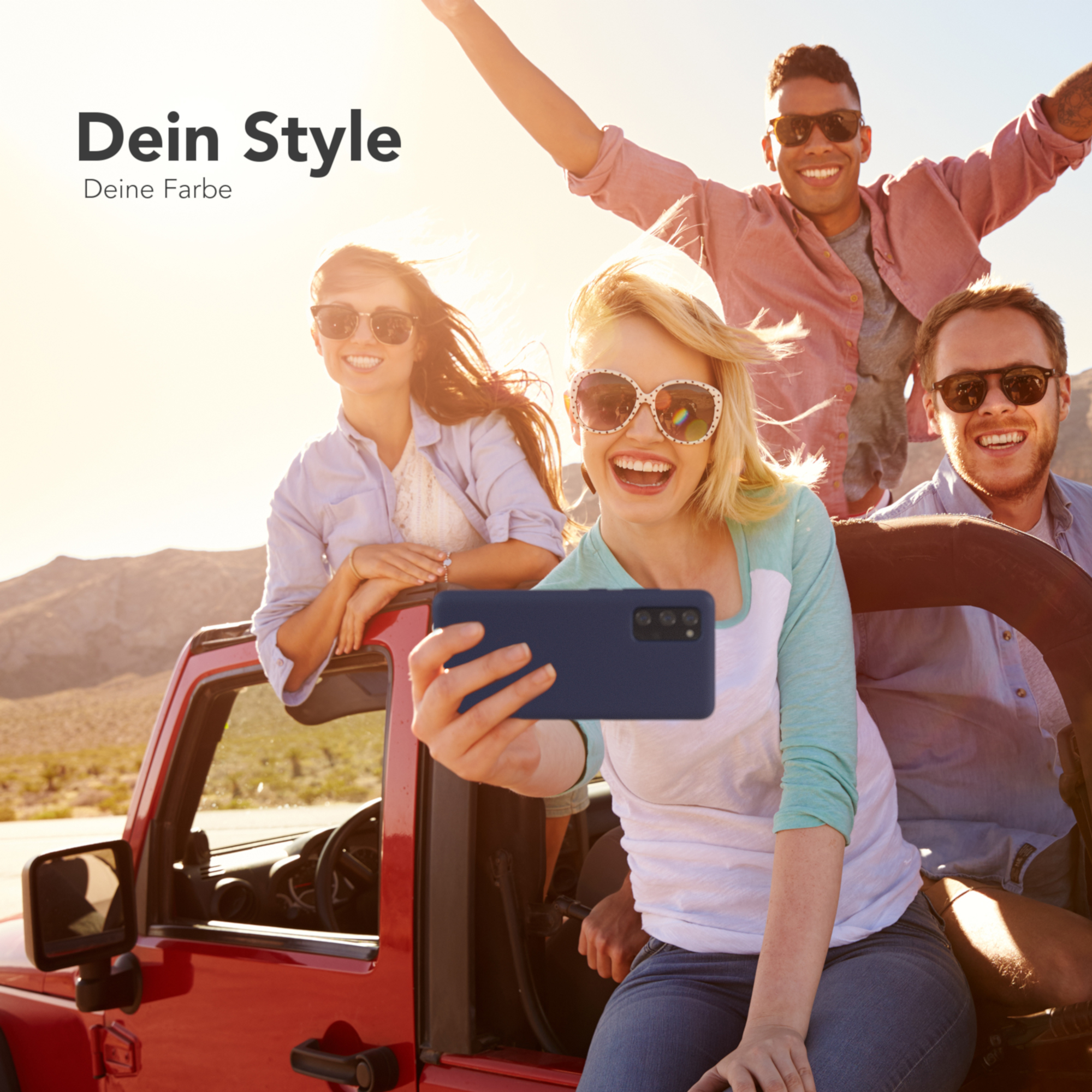Vier Personen in einem roten Jeep machen ein Selfie, zeigen eine Handyhülle und genießen die Natur.