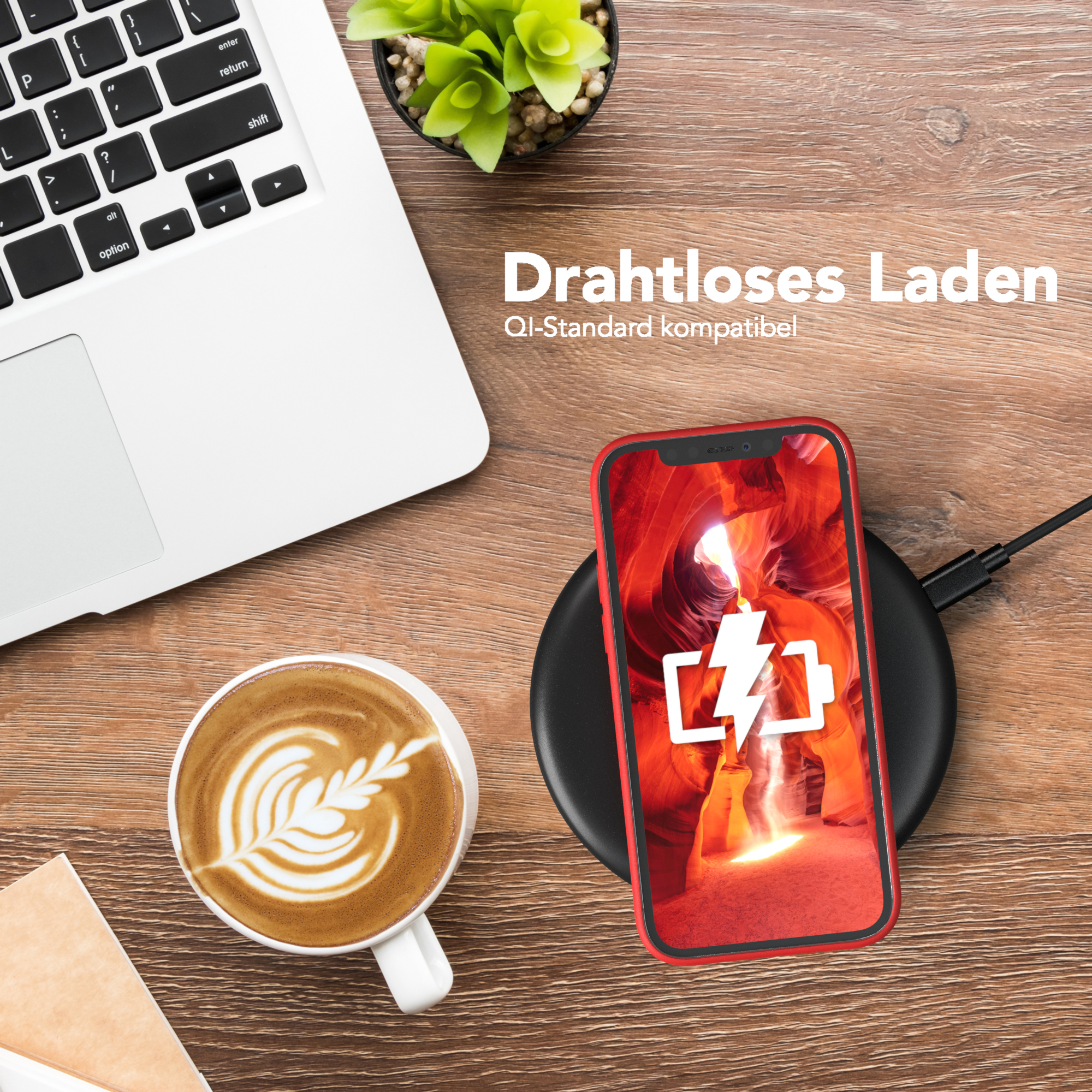 Ein Telefon, das drahtlos auf einem schwarzen Ladegerät geladen wird, neben einem Laptop und einer Kaffeetasse.