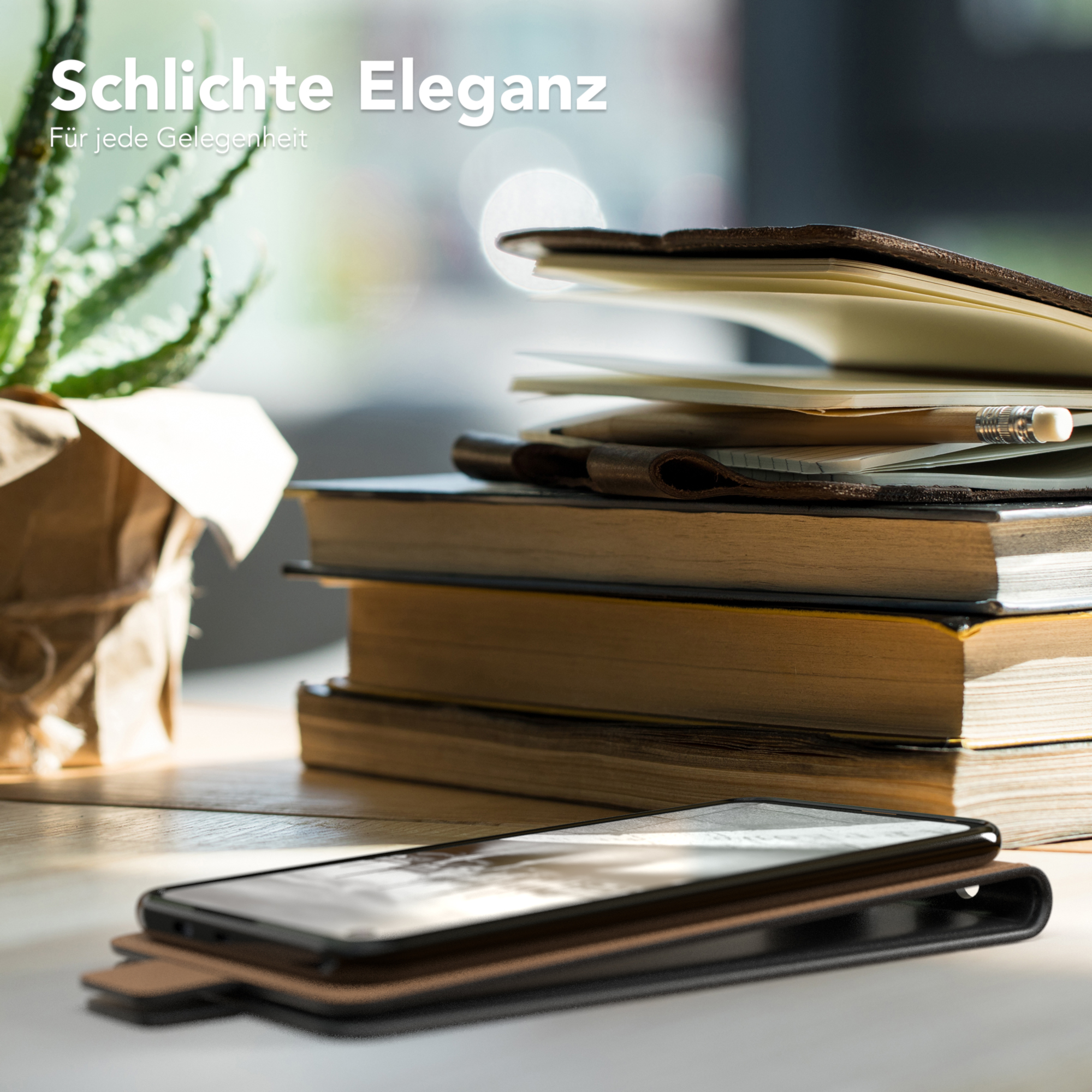 Telefon in einer braunen Lederhülle auf einem Holztisch, mit Büchern, einer Pflanze und einem Bleistift im Hintergrund.