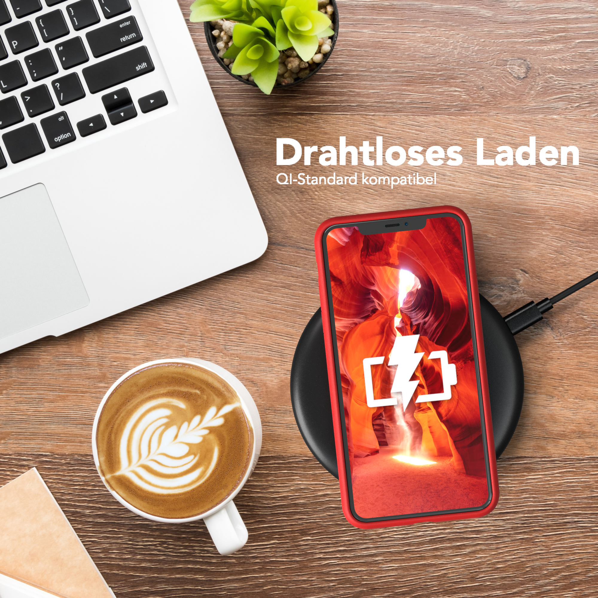 Telefon, der auf einem kabellosen Ladegerät liegt, neben einem Laptop und einer Kaffeetasse mit Latte Art, auf einem Holztisch.