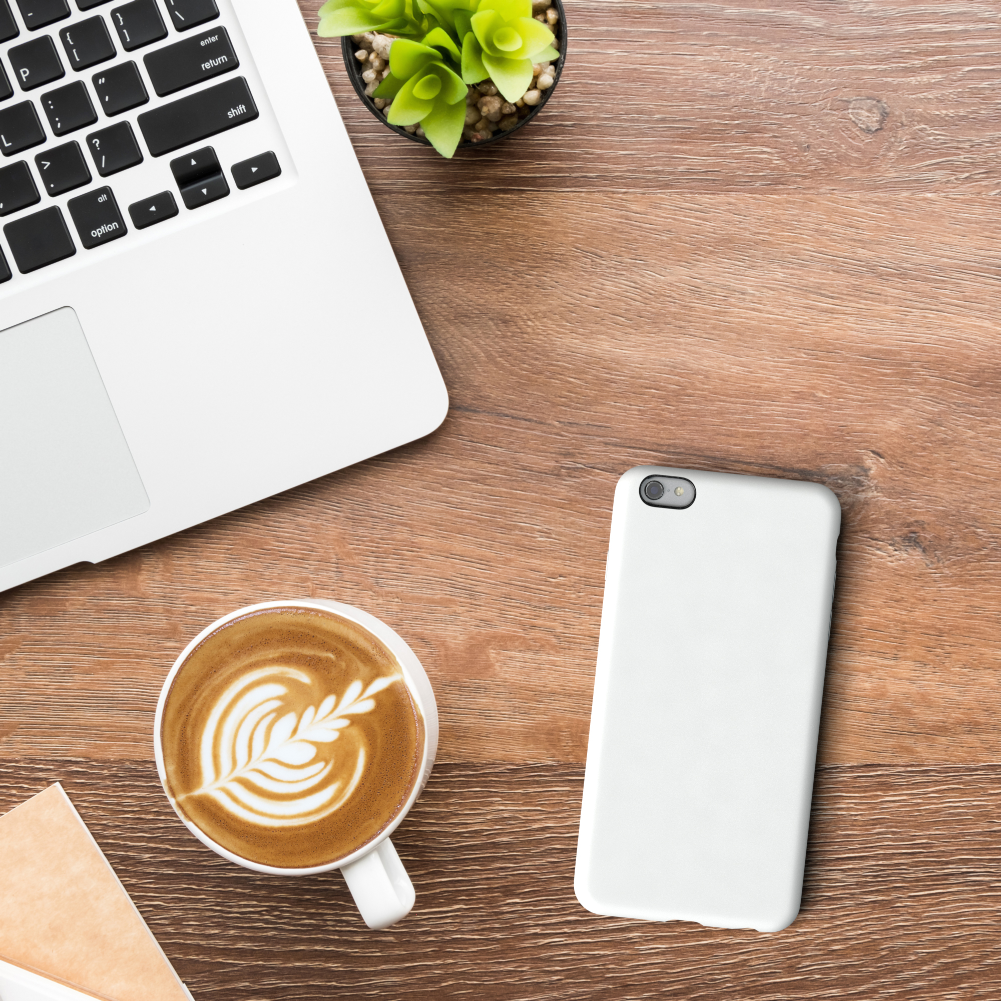 Laptop, Kaffee mit Latte Art und eine Handyhülle auf einem Holztisch. Draufsicht.
