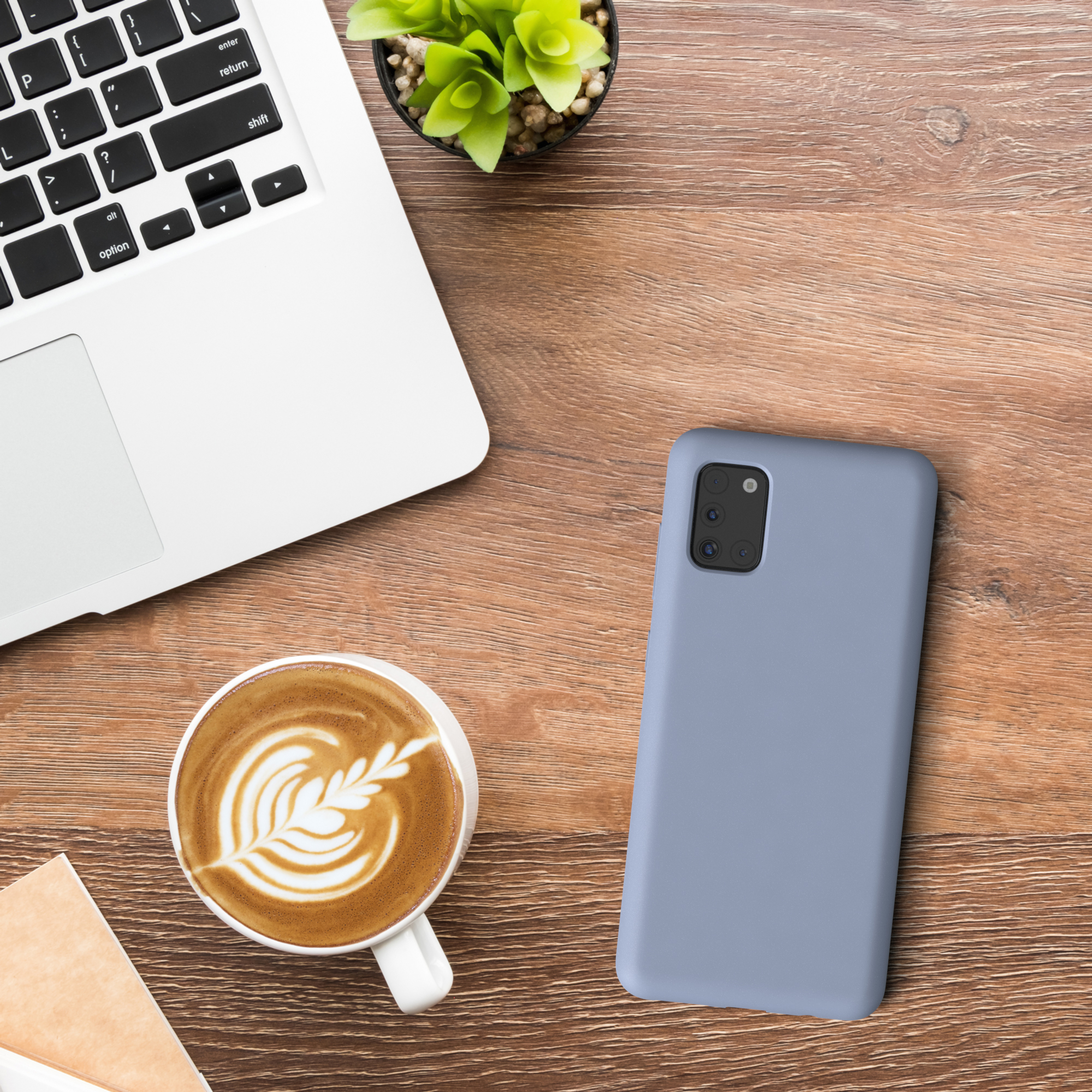 Laptop, Kaffee mit Latte Art, eine kleine Pflanze und ein blaues Telefon liegen auf einem Holztisch.