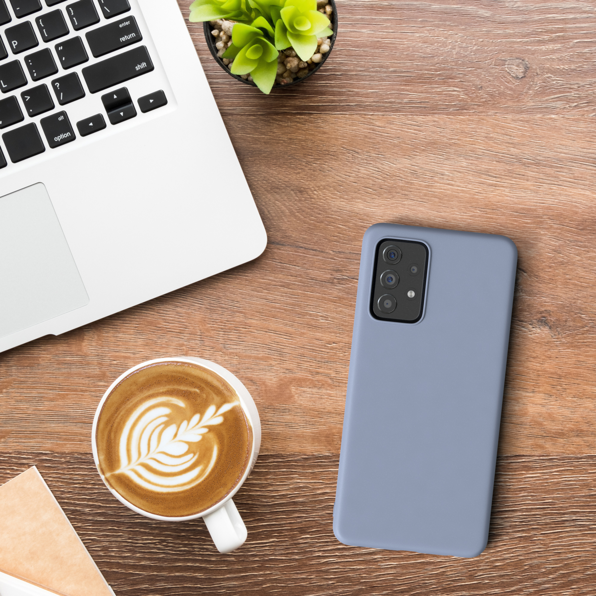 Ein Laptop, eine Kaffeetasse mit Latte Art, ein Telefon und eine kleine Pflanze auf Holztisch.