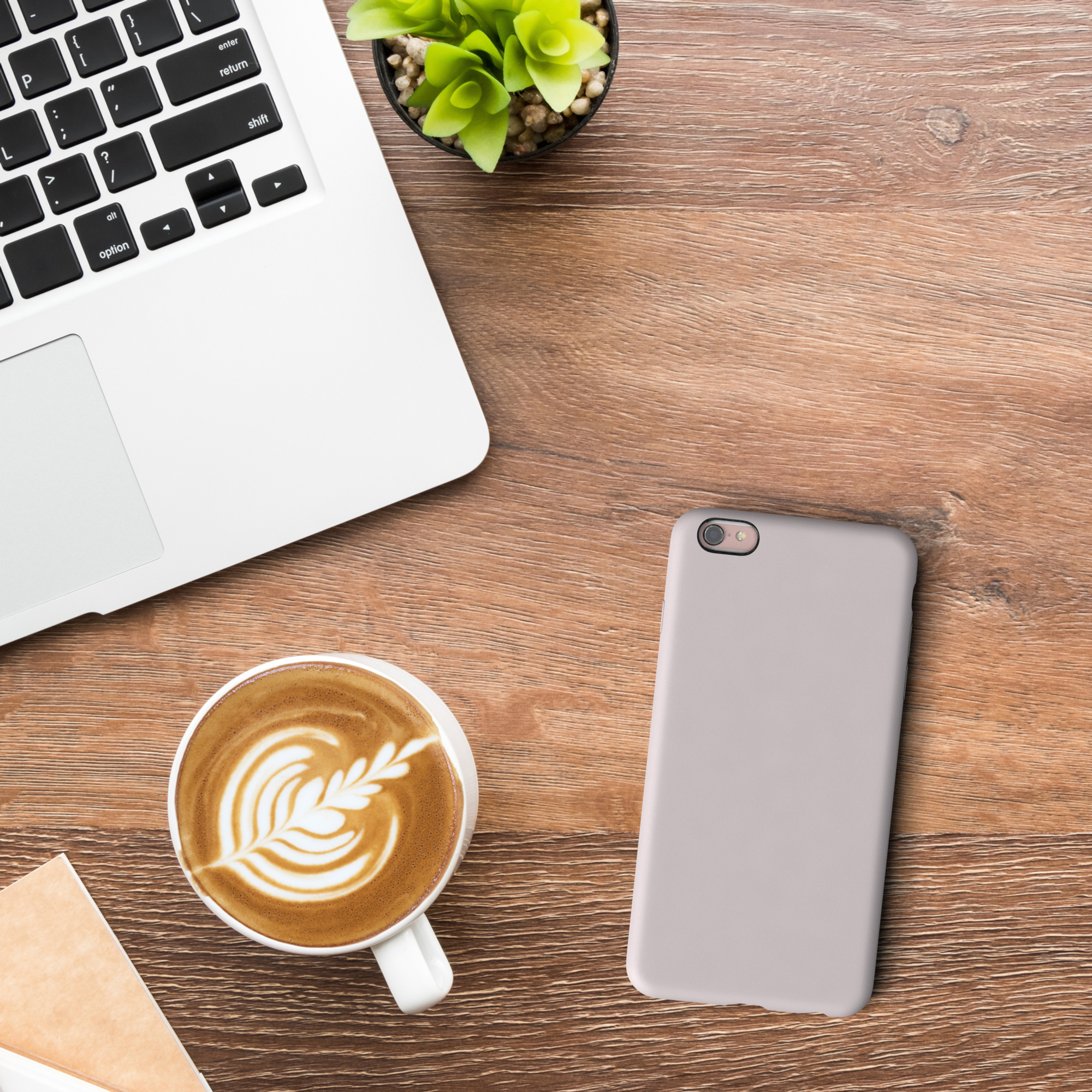Laptop, Telefon mit hellfarbiger Hülle und Kaffee mit Latte Art auf einem Holztisch.