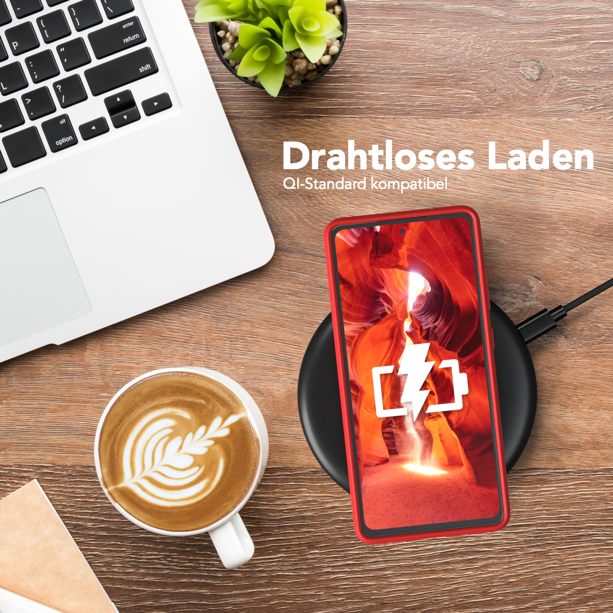Telefon auf kabellosem Ladegerät, neben Laptop, Kaffee und Pflanze.