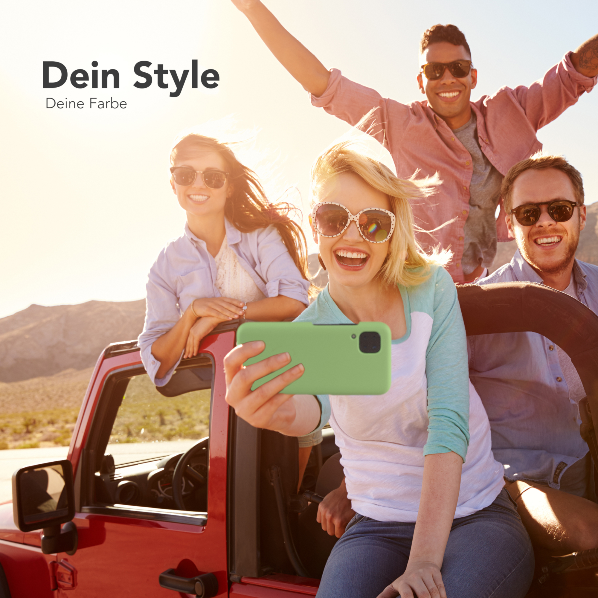 Vier Personen in einem roten Jeep machen ein Selfie. Berge im Hintergrund, helles Sonnenlicht. Zwei Personen tragen Sonnenbrillen.