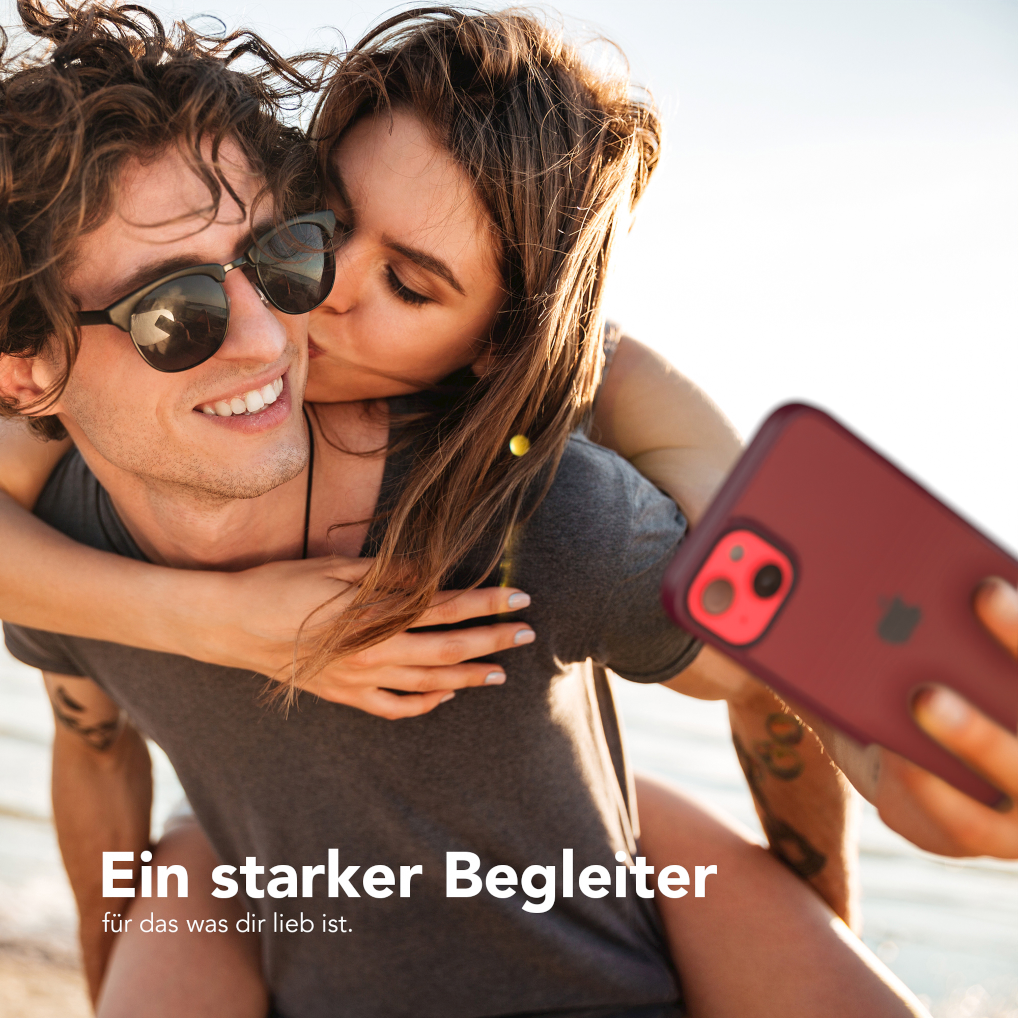Ein Paar macht ein Selfie. Die Frau küsst den Mann auf die Wange. Der Mann hält ein Telefon.