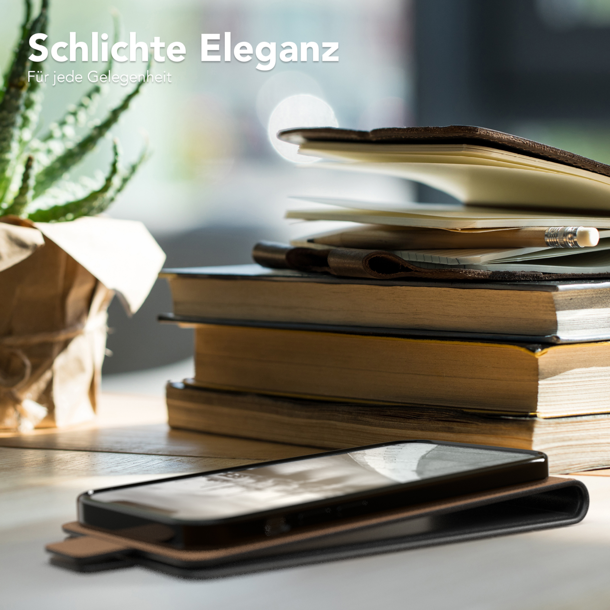 Eine Handyhülle mit braunem Lederbezug liegt auf einem Tisch mit Büchern, einer Pflanze und einem Telefon.