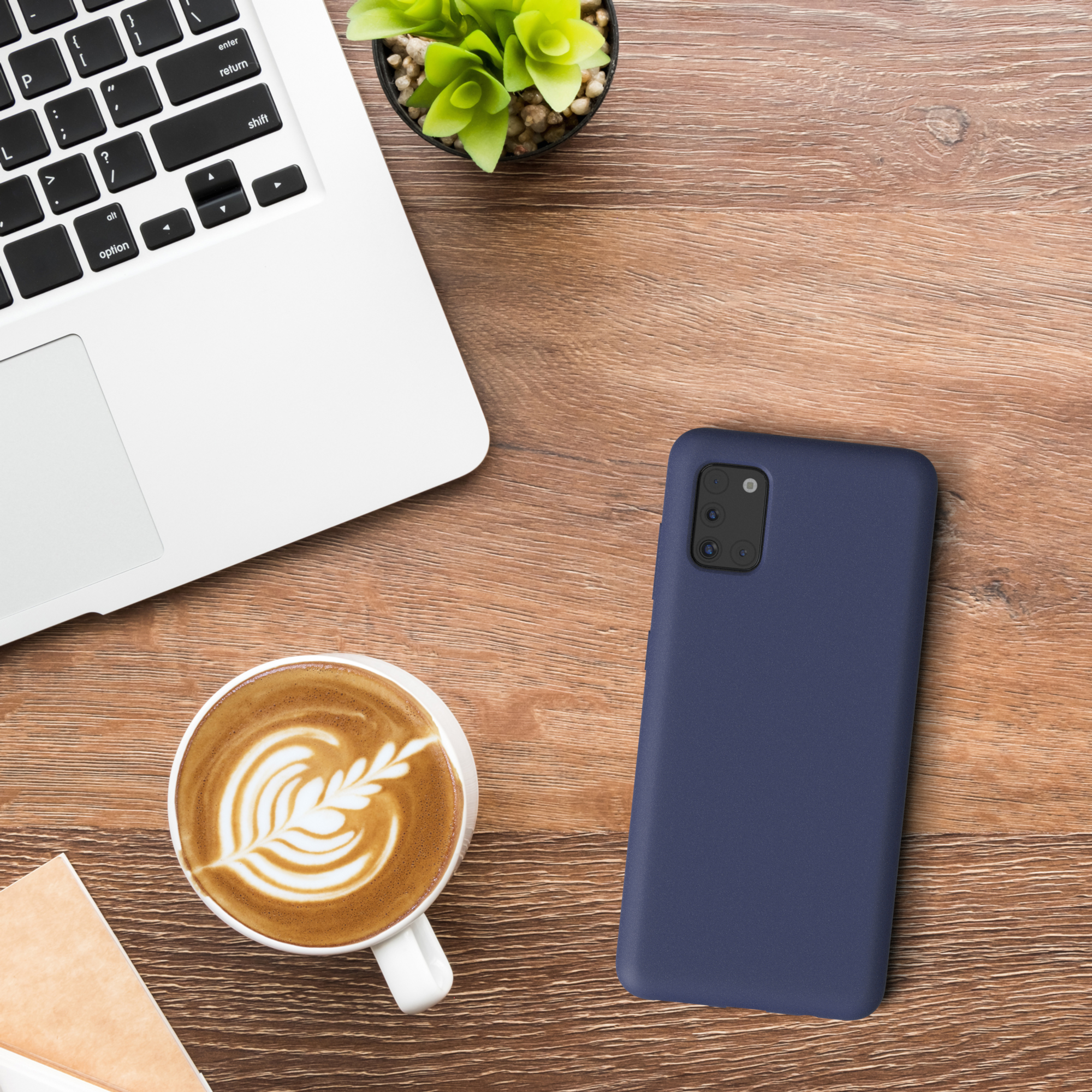 Laptop, Kaffeetasse mit Latte Art und eine Handyhülle auf einem Holztisch. Grüne Pflanze.