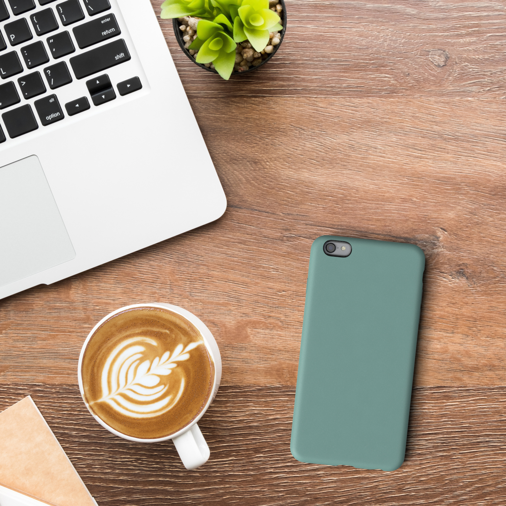Ein Laptop, eine Tasse Kaffee mit Latte Art und eine Handyhülle auf einem Holztisch.