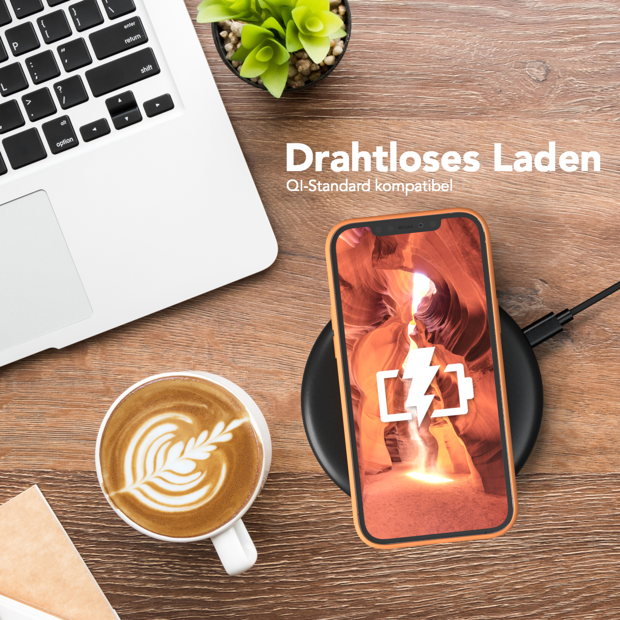 Ein Telefon auf einem kabellosen Ladegerät, ein Laptop und eine Tasse Kaffee auf einem Holztisch. Eine Pflanze ist auch vorhanden.