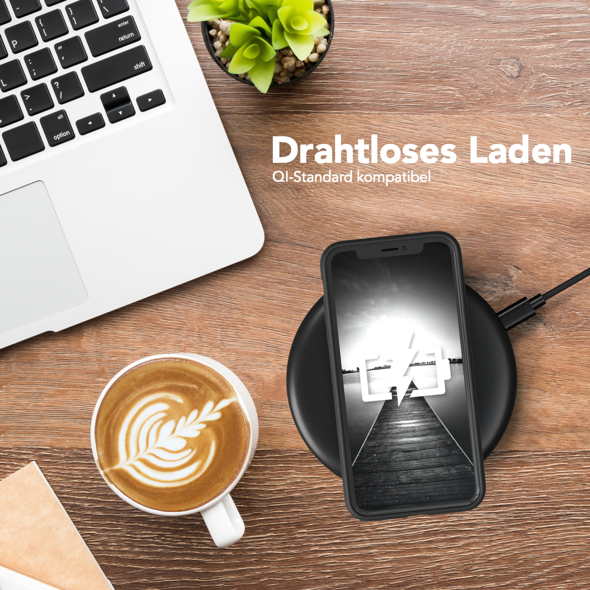 Ein Telefon auf einem kabellosen Ladegerät, ein Laptop und eine Kaffeetasse mit Latte Art auf einem Holztisch. Pflanze.