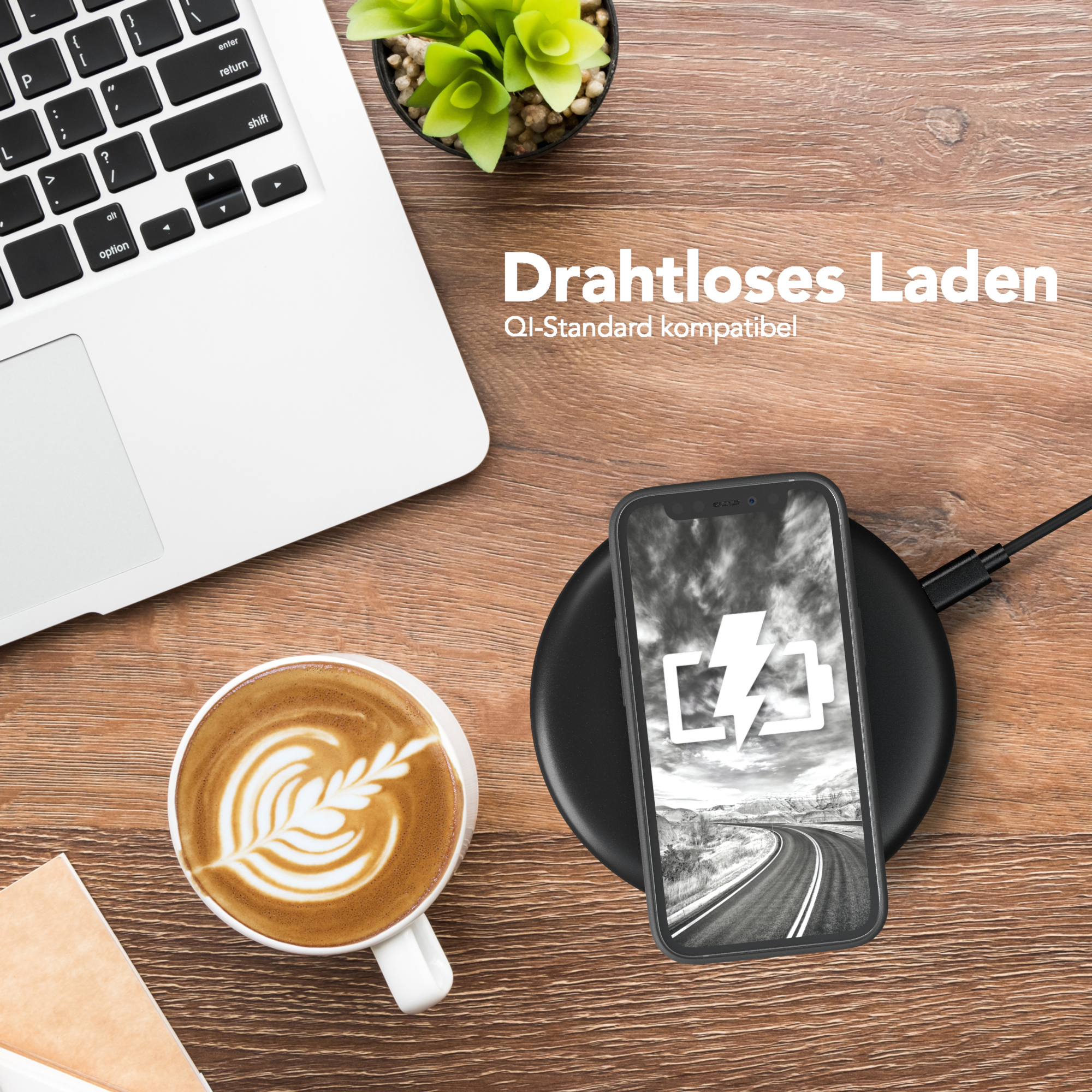 Ein Laptop, eine Kaffeetasse mit Kunst und ein Telefon, das auf einem kabellosen Ladegerät auf einem Holztisch geladen wird.