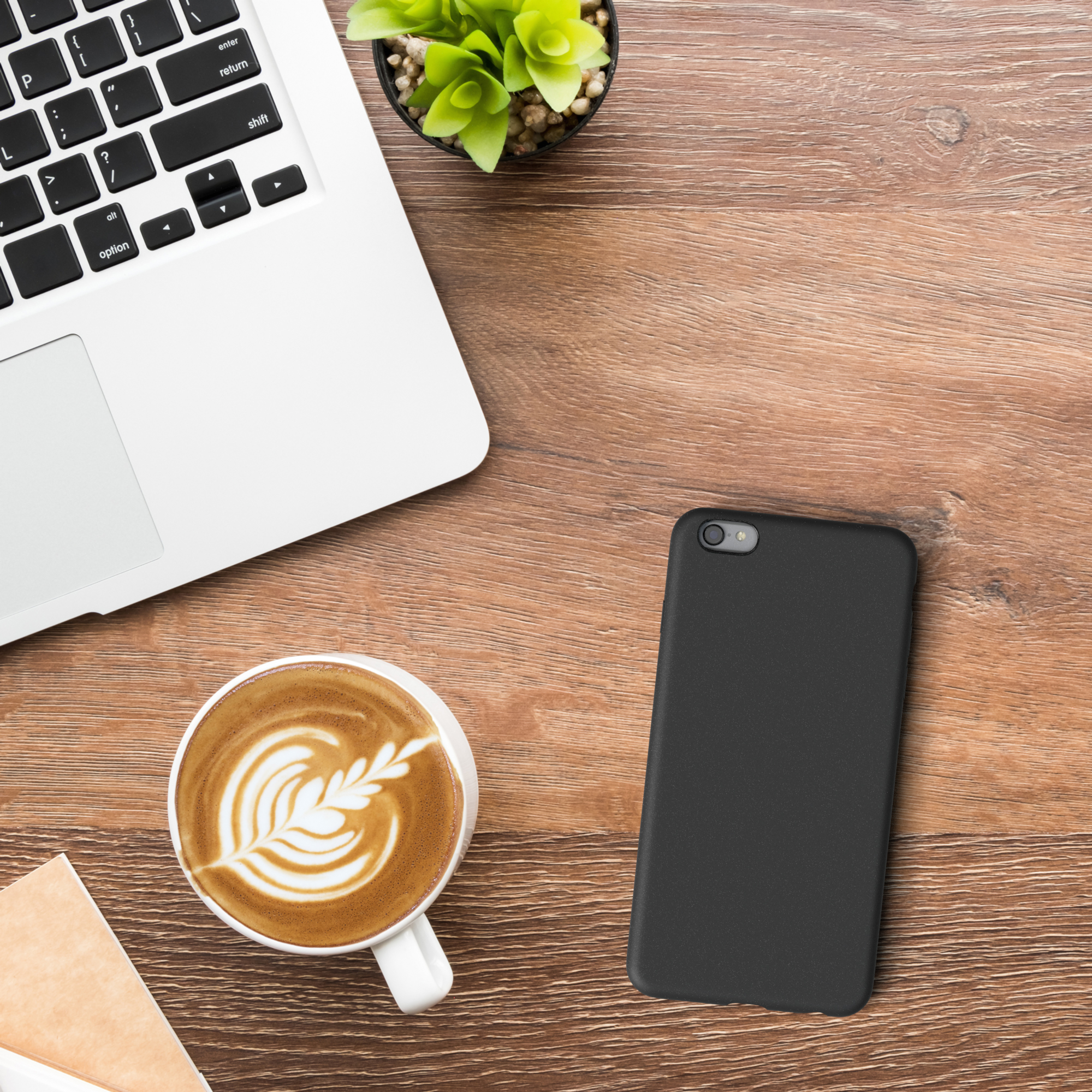 Laptop, Kaffee mit Latte Art, schwarzes Telefon und Pflanze auf Holzschreibtisch.