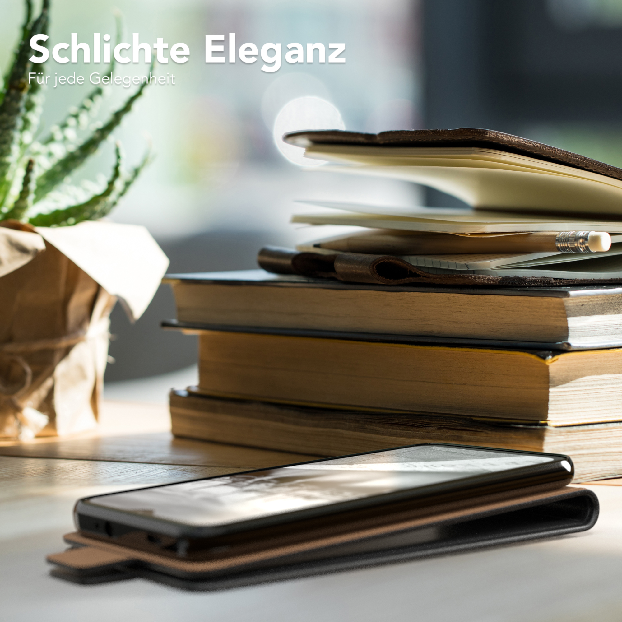 Telefon in brauner Hülle auf Schreibtisch mit Büchern und Pflanze. Text: Schlichte Eleganz.