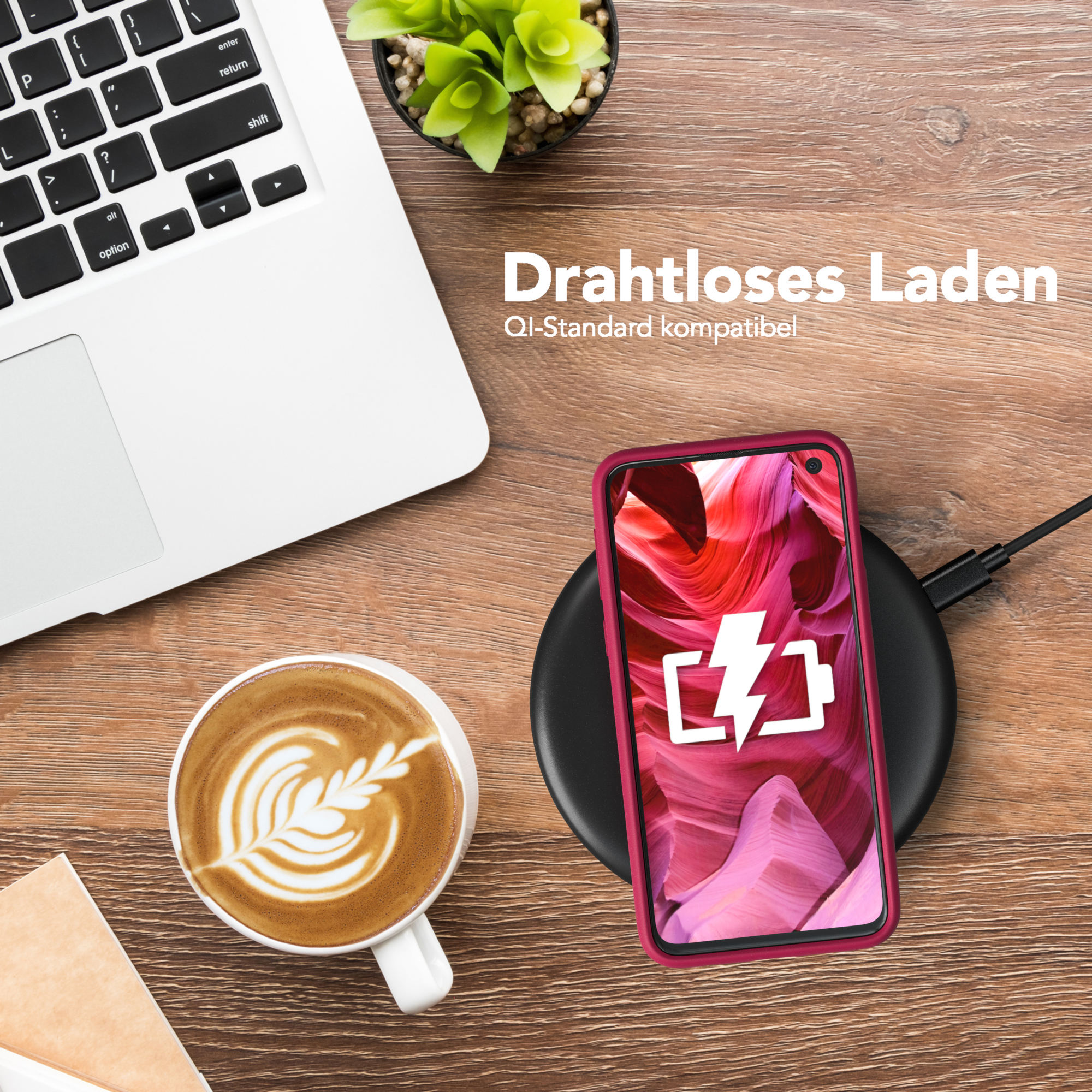 Ein Telefon auf einem kabellosen Ladegerät, ein Laptop und eine Kaffeetasse mit Latte Art auf einem Holztisch. Pflanze.