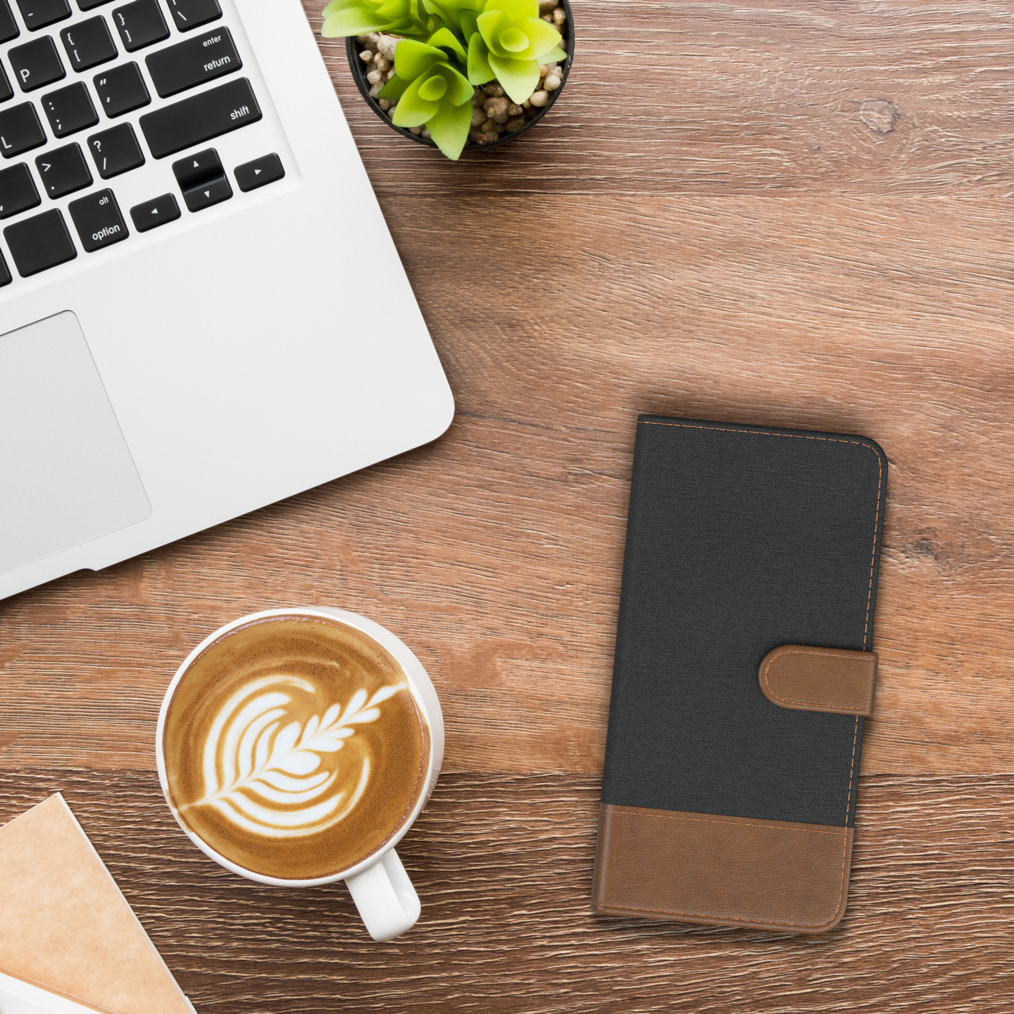 Laptop, Kaffeetasse mit Kunst, schwarze und braune Handyhülle auf einem Holztisch.