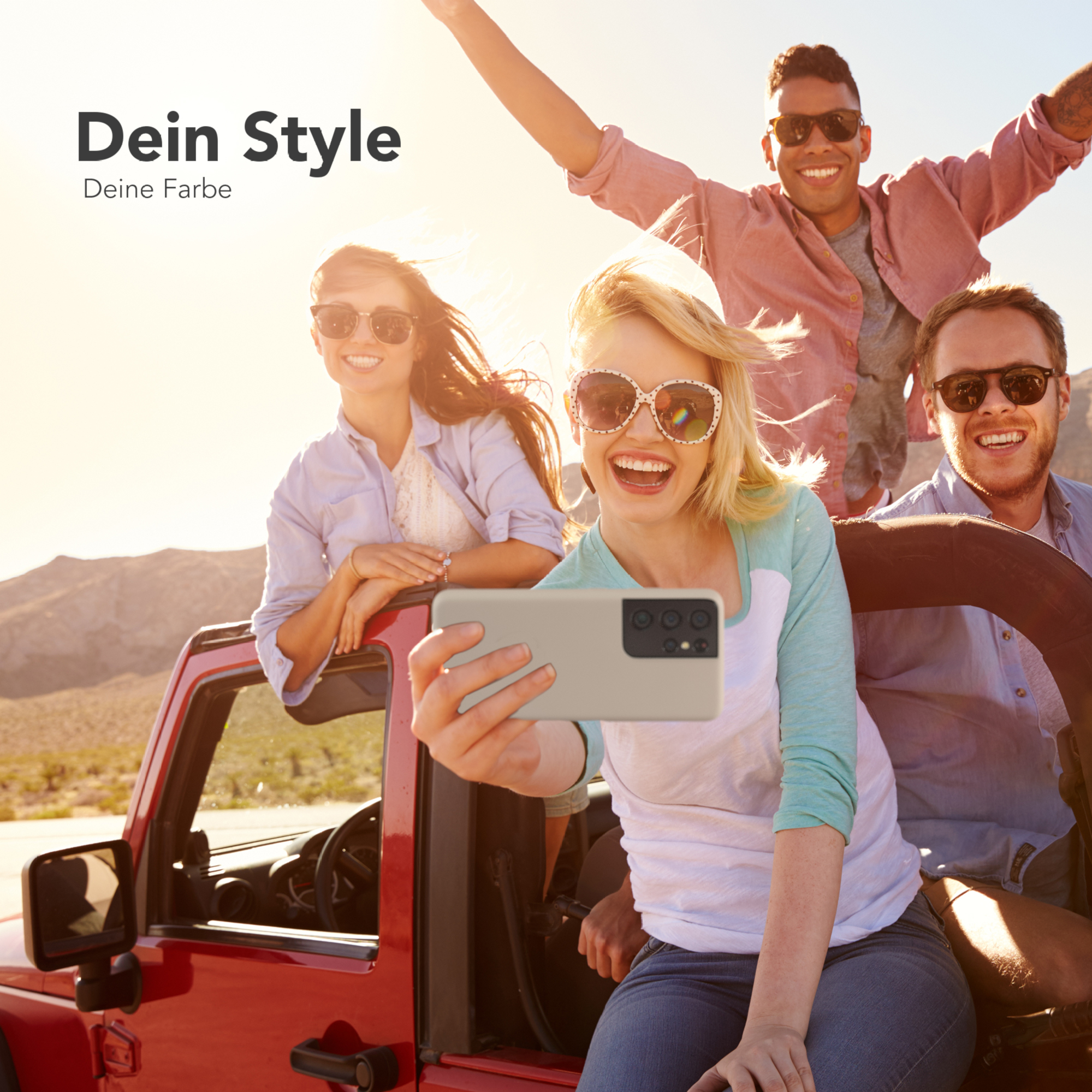 Vier Personen in einem roten Jeep machen ein Selfie mit einem Telefon. Wüste im Hintergrund.
