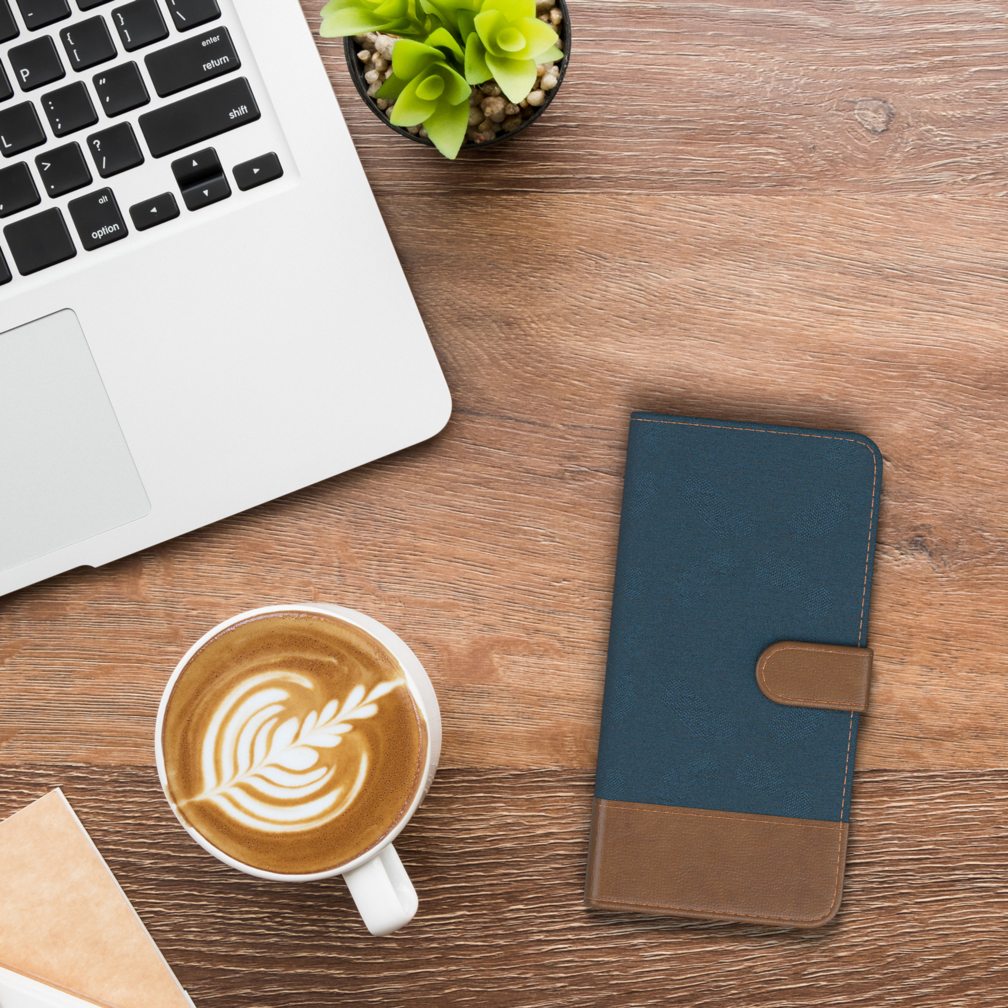 Laptop, Kaffee und Notizbuch auf einem Holzschreibtisch. Eine blau-braune Handyhülle liegt rechts.