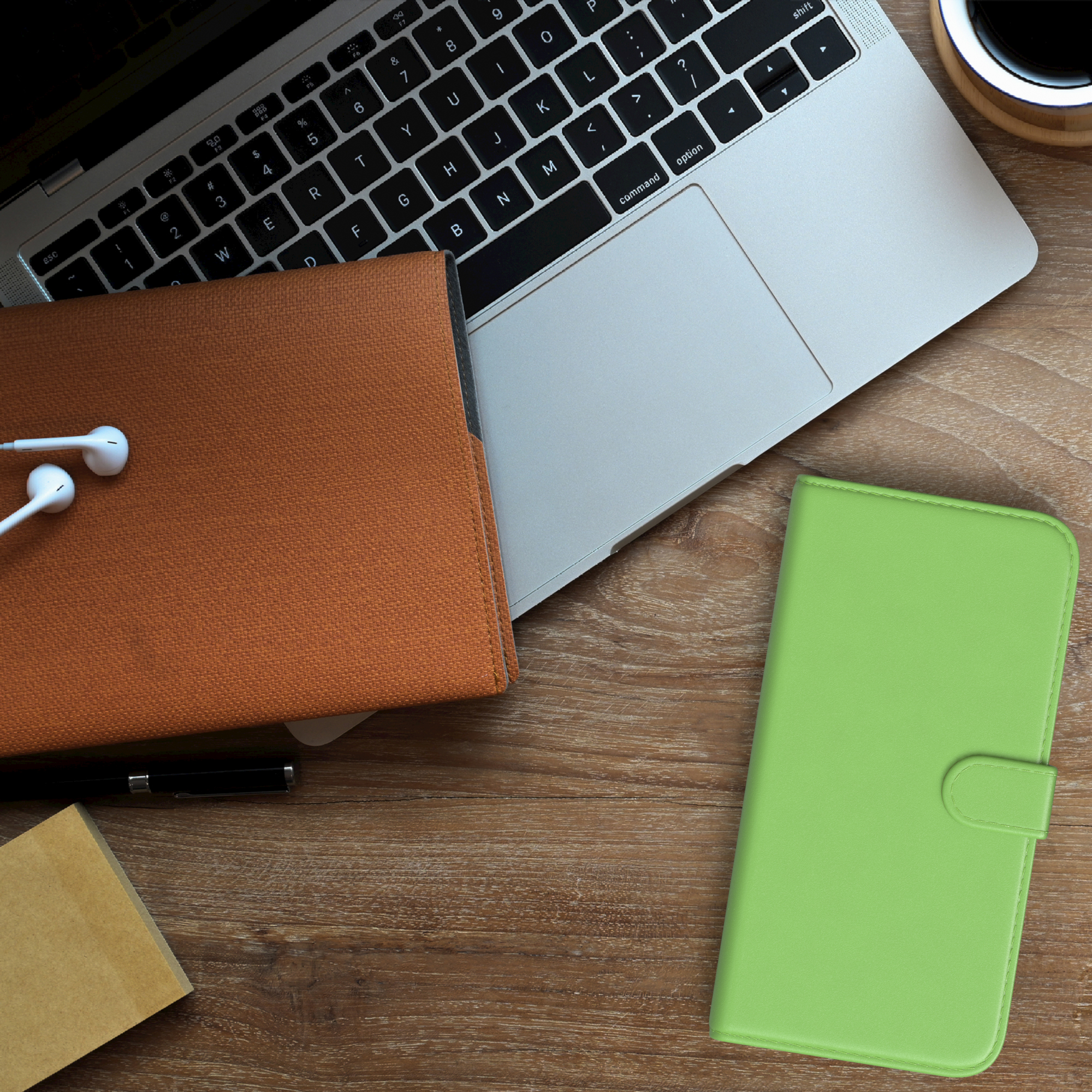 Laptop, braune Hülle, grüne Hülle und Kopfhörer auf einem Holztisch.