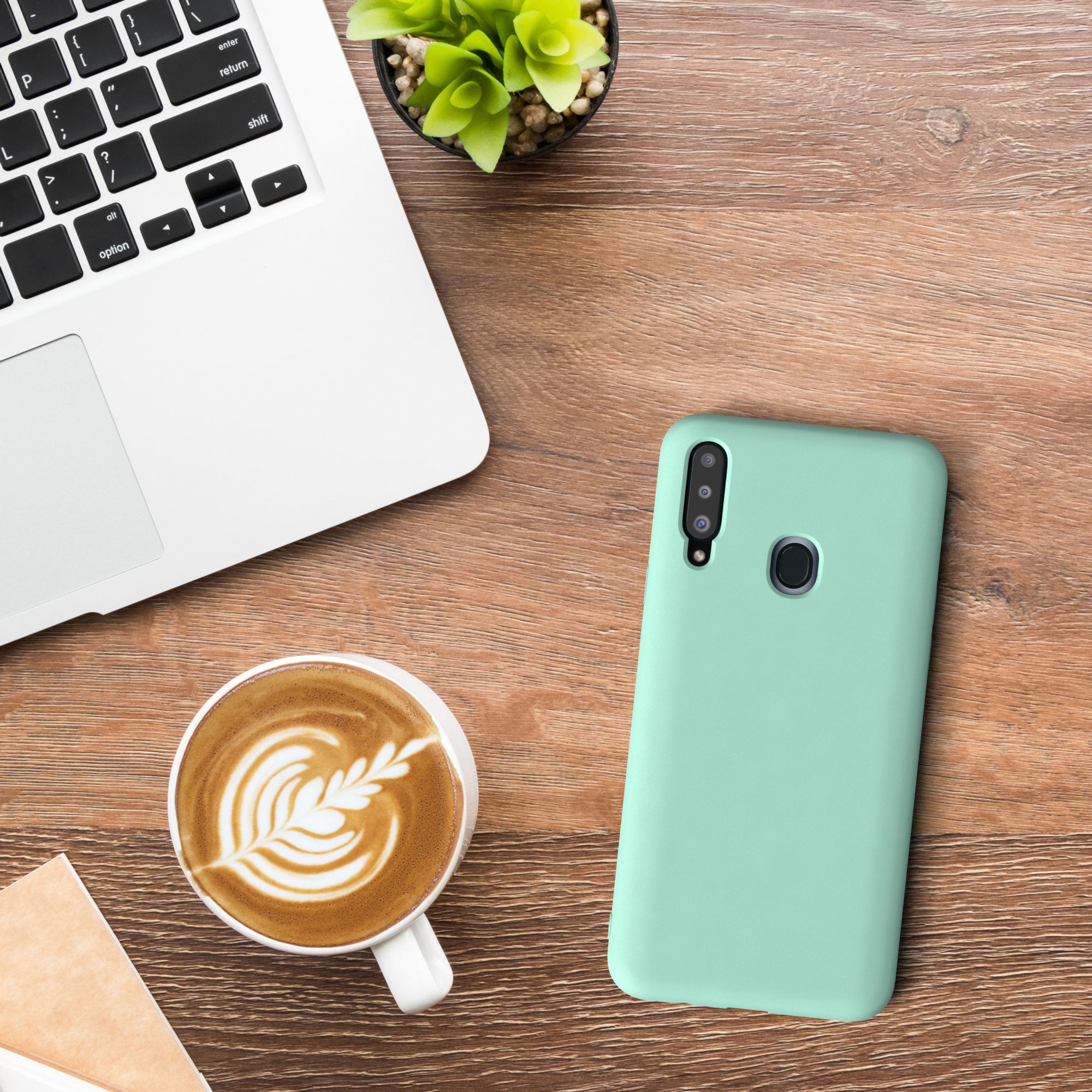 Eine Handyhülle, Kaffee, Laptop und Pflanze auf einem Holztisch. Die Handyhülle ist hellgrün.