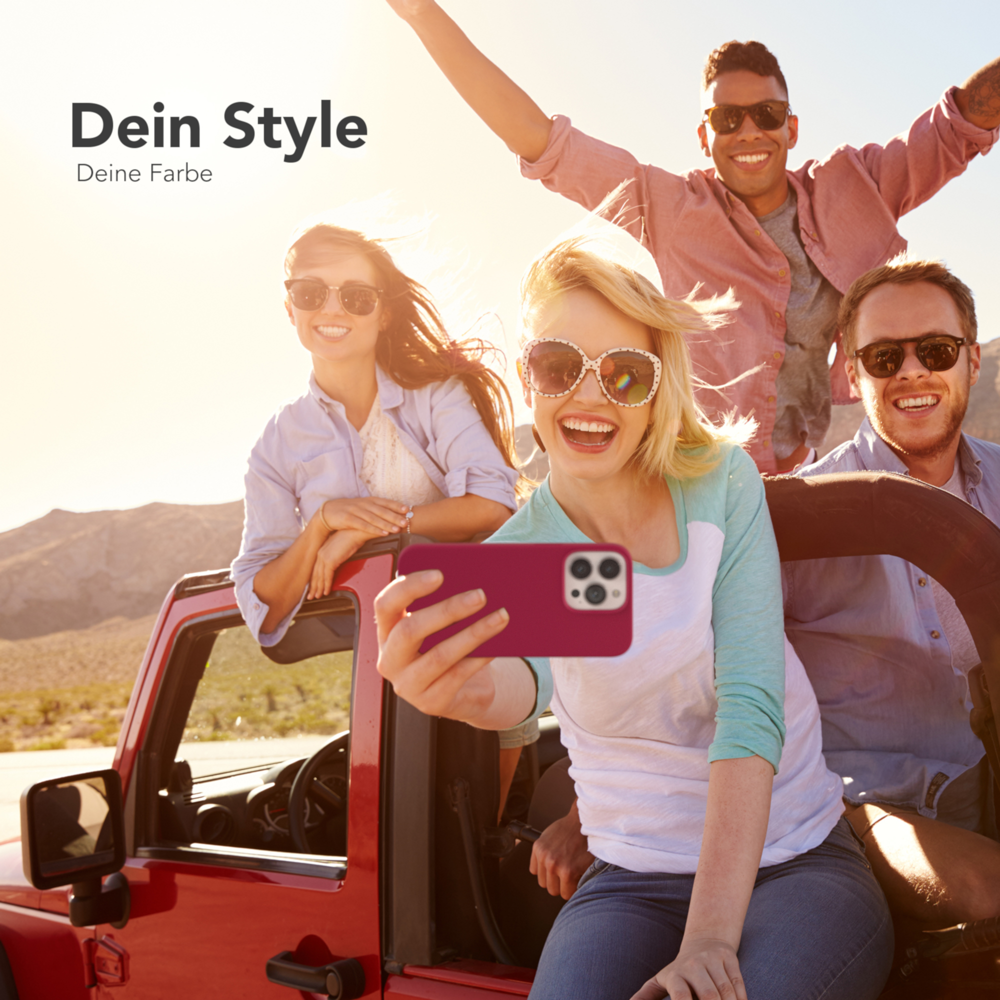 Vier Personen in einem roten Jeep machen ein Selfie mit einer rosa Handyhülle und lächeln in der Sonne.
