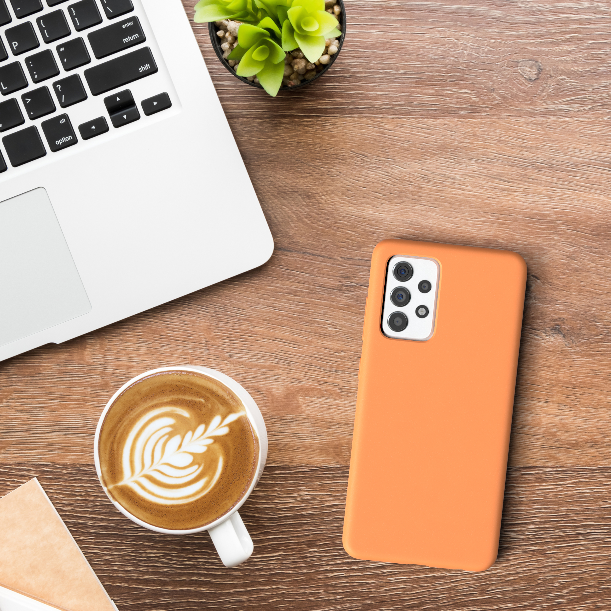 Ein Telefon in einer orangefarbenen Hülle auf einem Holzschreibtisch, mit Laptop und Kaffeetasse.