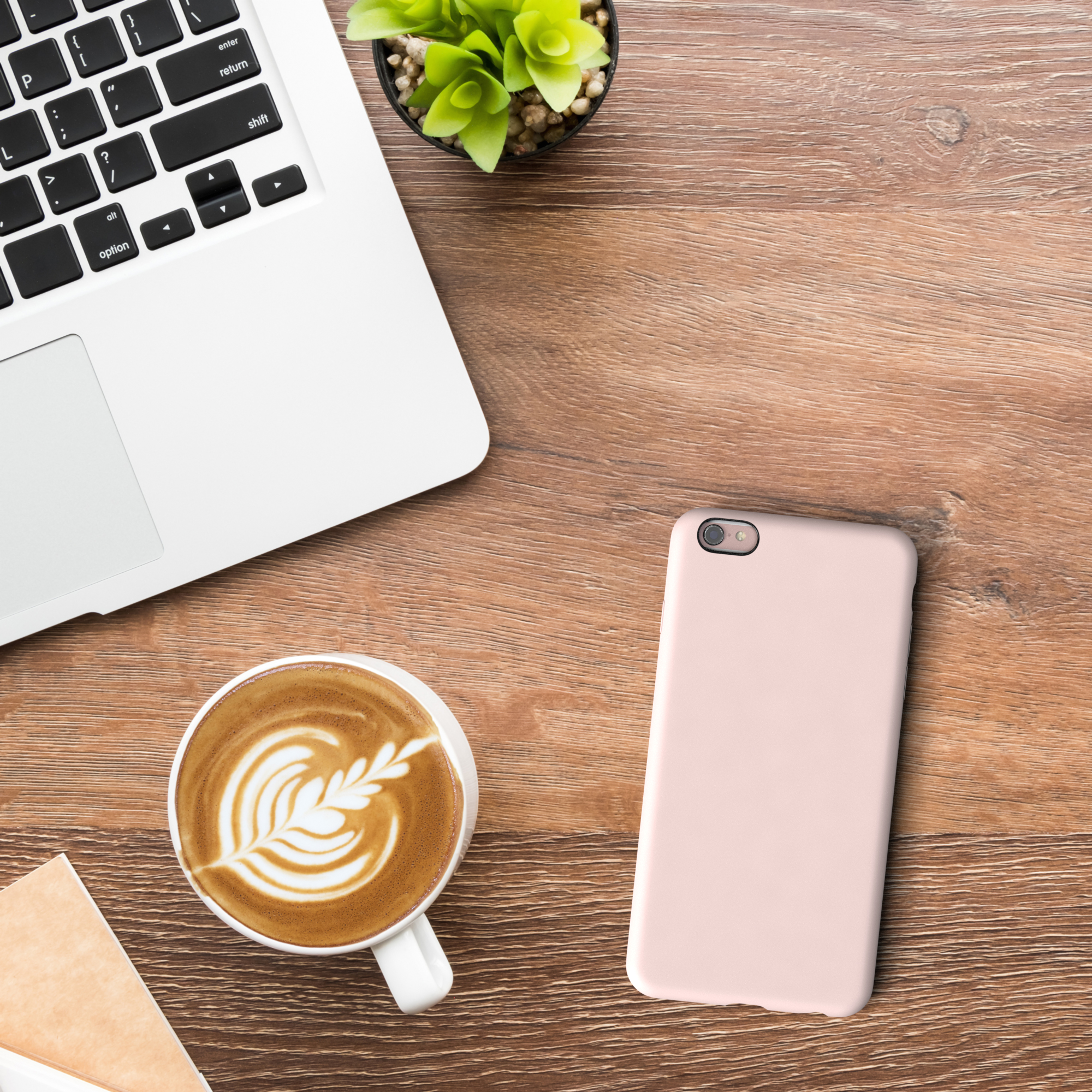Laptop, Kaffee mit Latte Art, rosa Handyhülle und eine kleine Pflanze auf Holz.