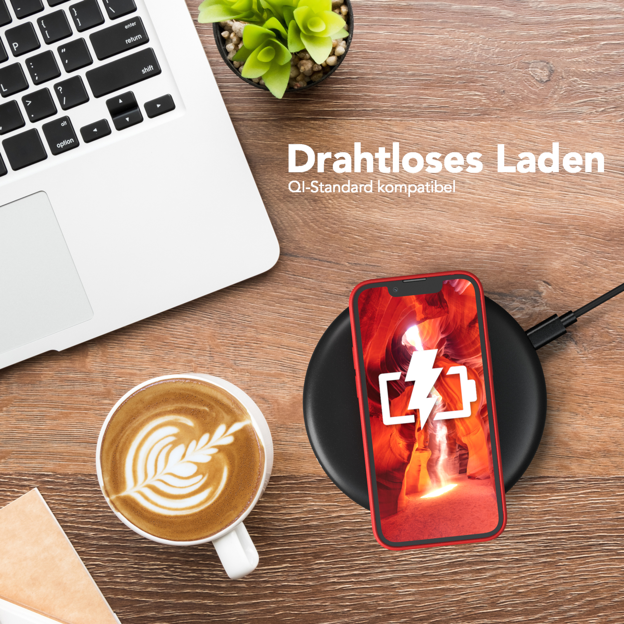 Telefon lädt auf schwarzem Pad. Laptop und Kaffeetasse auf Holzoberfläche.