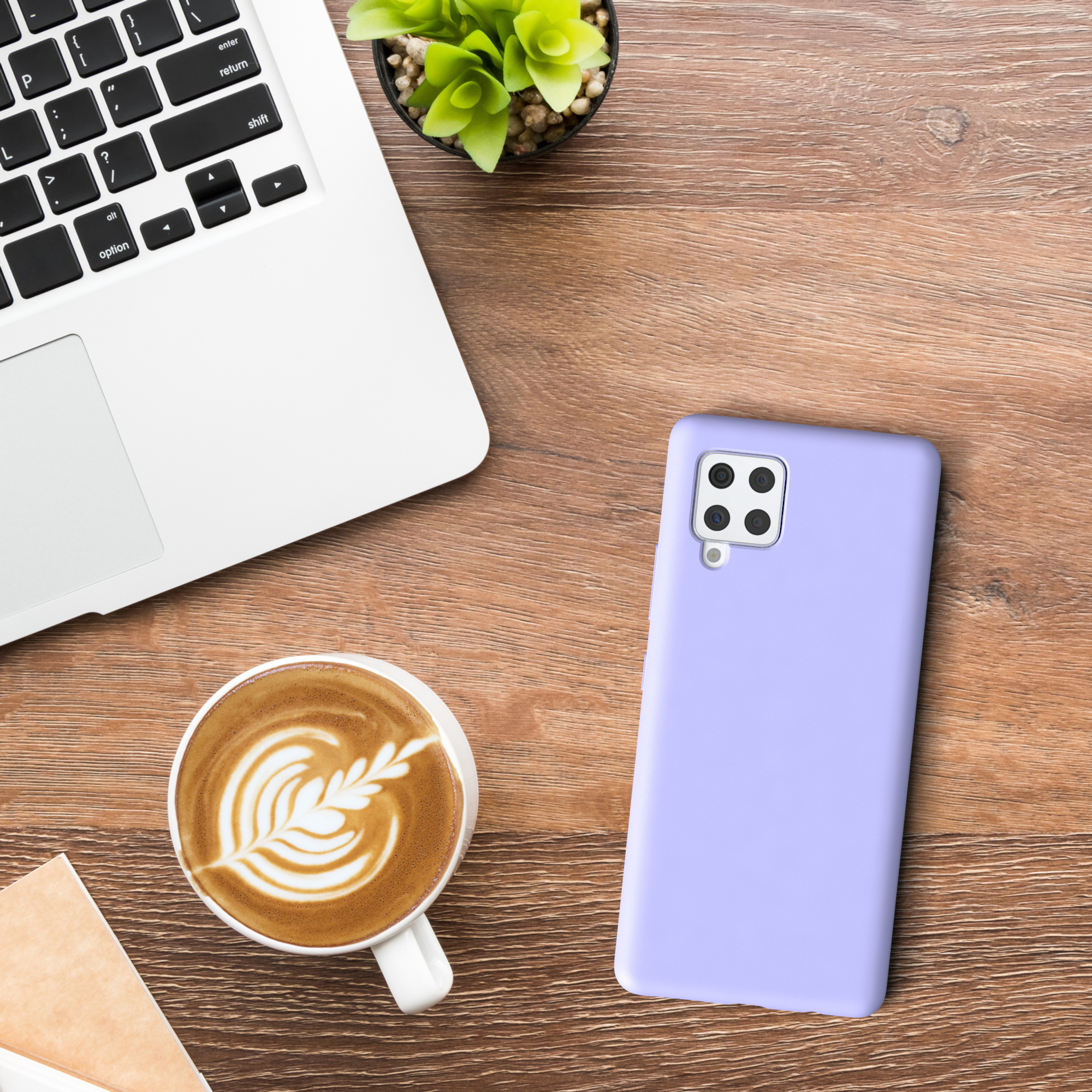 Ein Laptop, Kaffee mit Latte Art, eine lila Handyhülle und eine kleine Pflanze auf einem Holztisch.