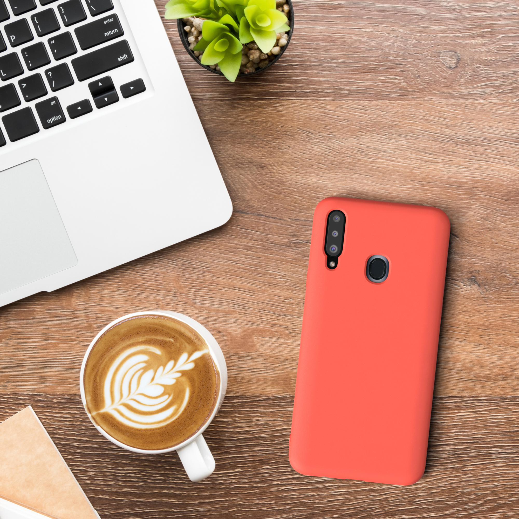 Laptop, Kaffee, kleine Pflanze und eine rote Handyhülle auf einem Holztisch.