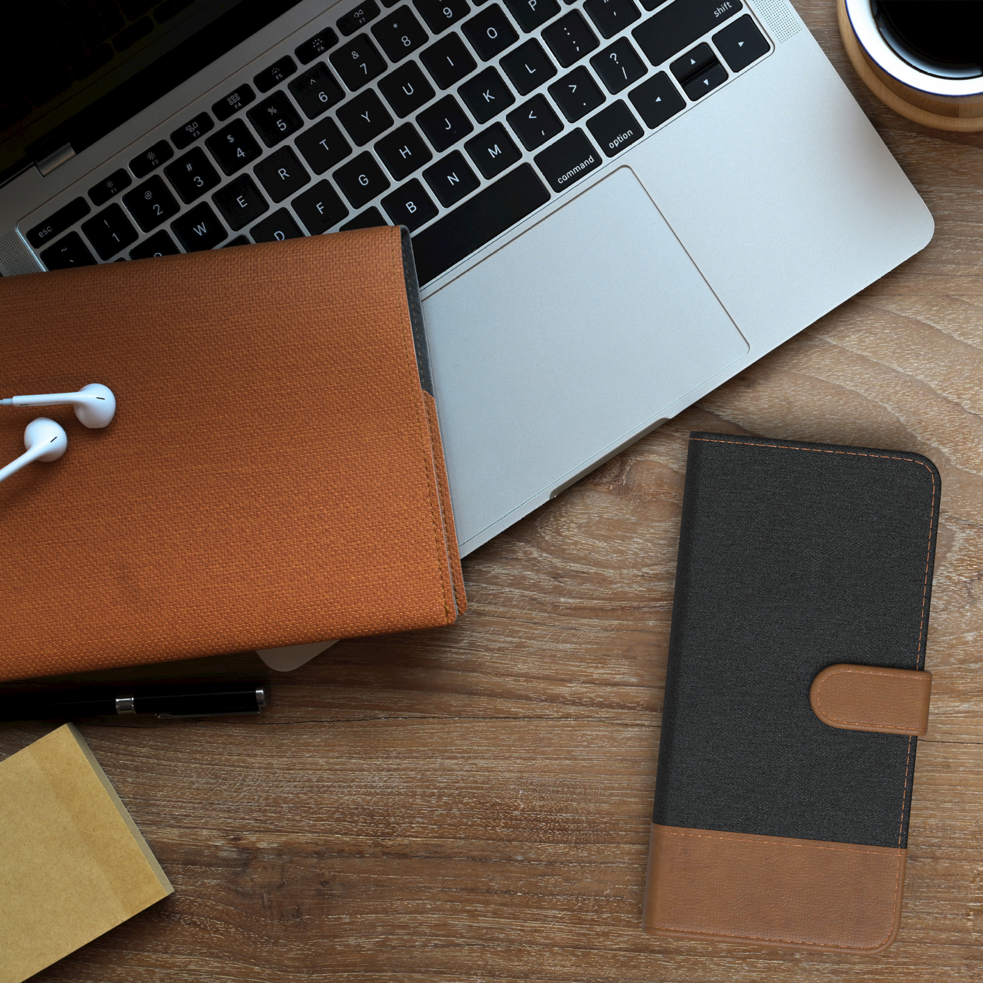 Laptop, Handyhülle und Zubehör auf einem Holztisch. Kaffeetasse in der Nähe.