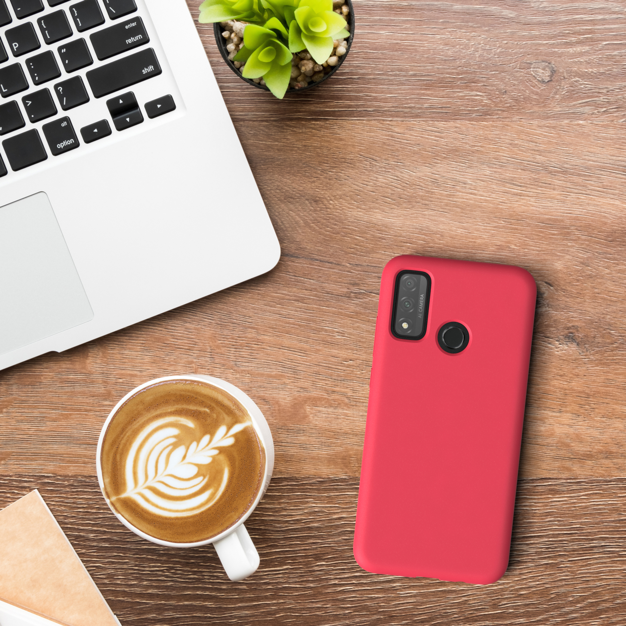 Eine rote Handyhülle auf einem Holztisch. Ein Laptop, Kaffee und eine Pflanze stehen auf dem Tisch.