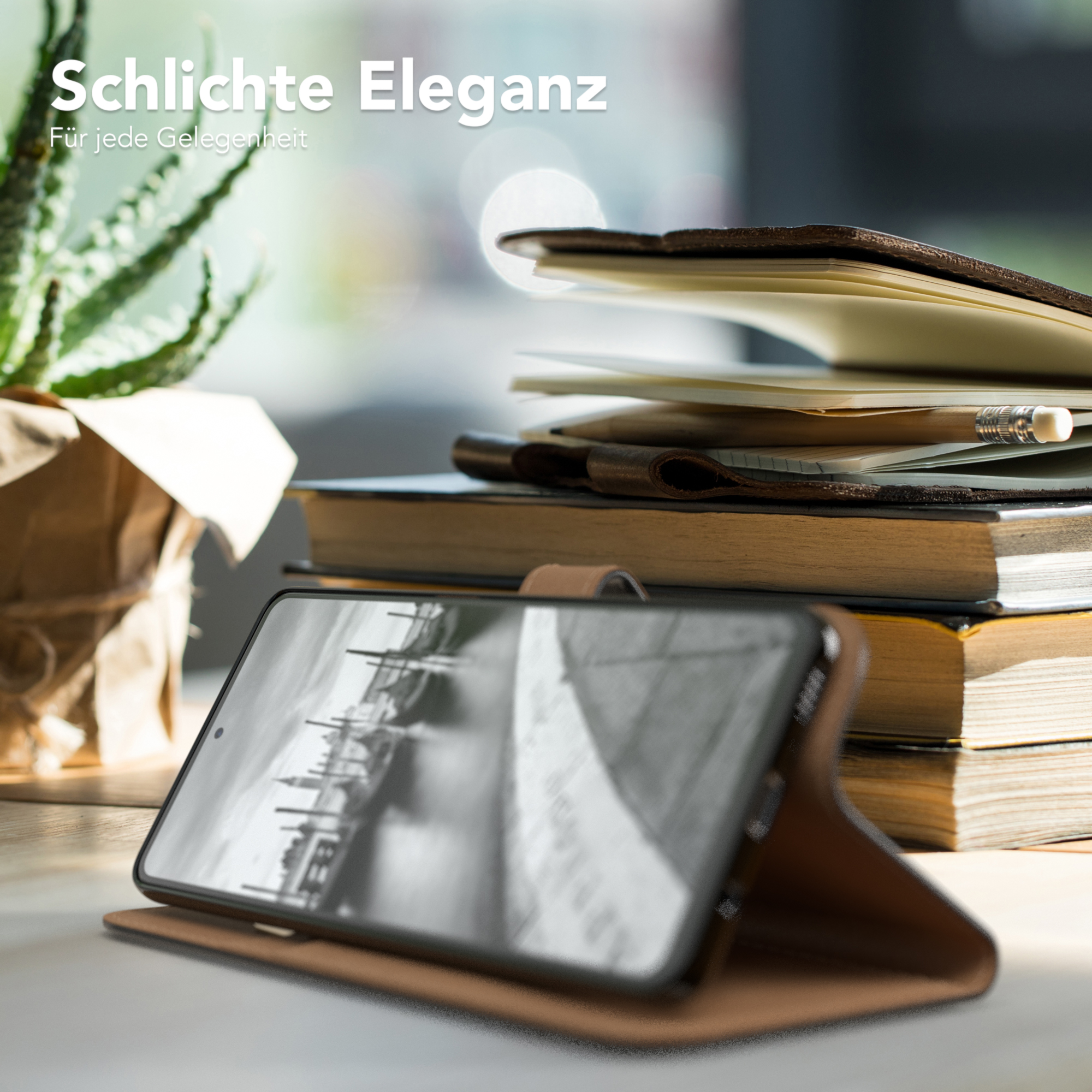 Ein Telefon in einer braunen Hülle liegt auf einem Tisch mit Büchern und einer kleinen Pflanze.