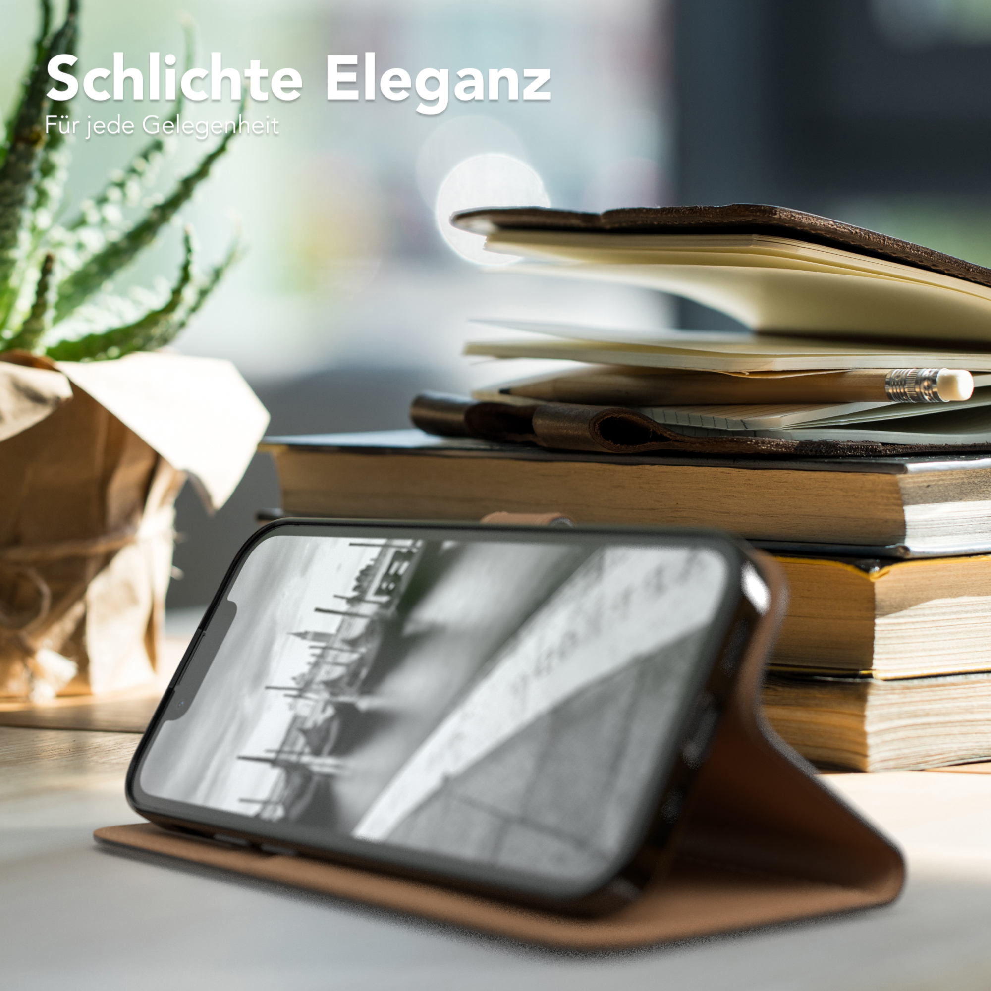 Telefon in brauner Hülle auf dem Schreibtisch, Bücher und Pflanze im Hintergrund.