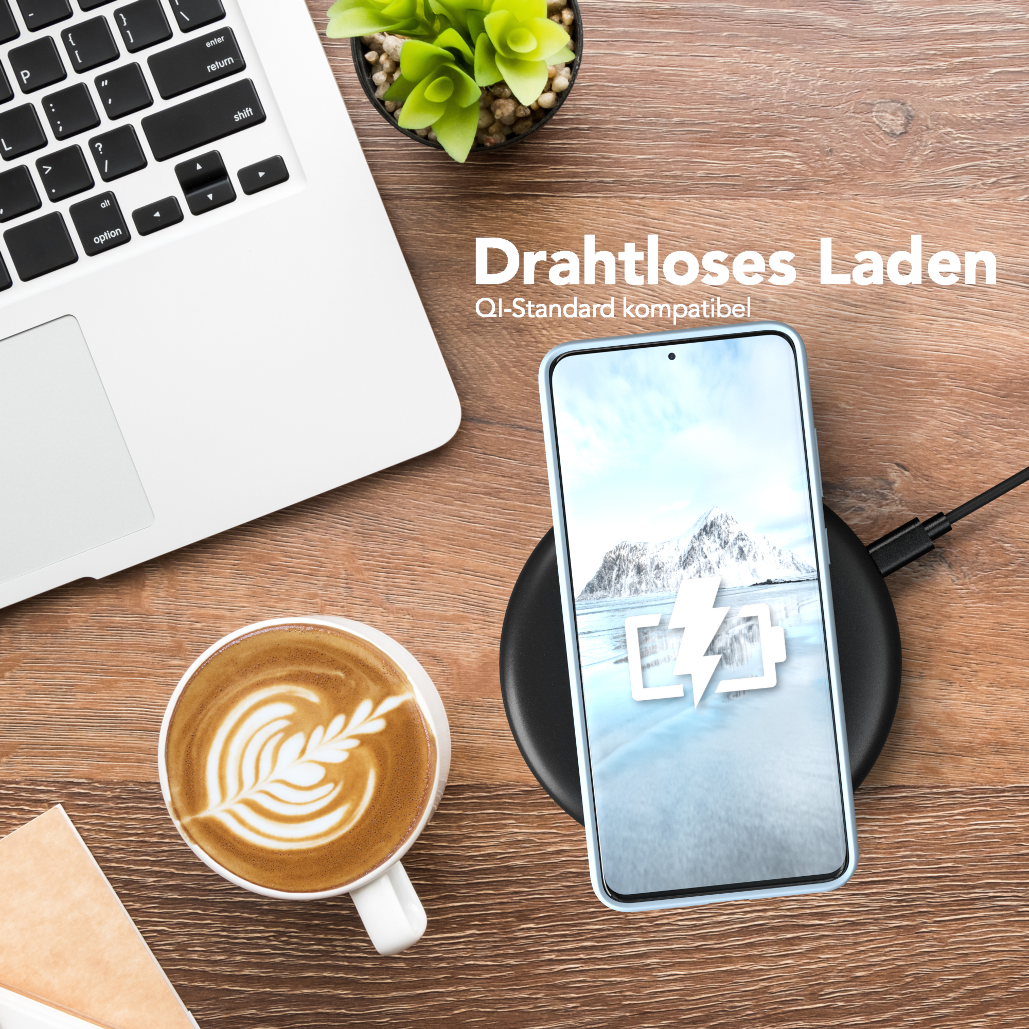 Telefon in einer Hülle auf einem kabellosen Ladepad, neben einem Laptop und einem Kaffee mit Latte Art auf Holz.