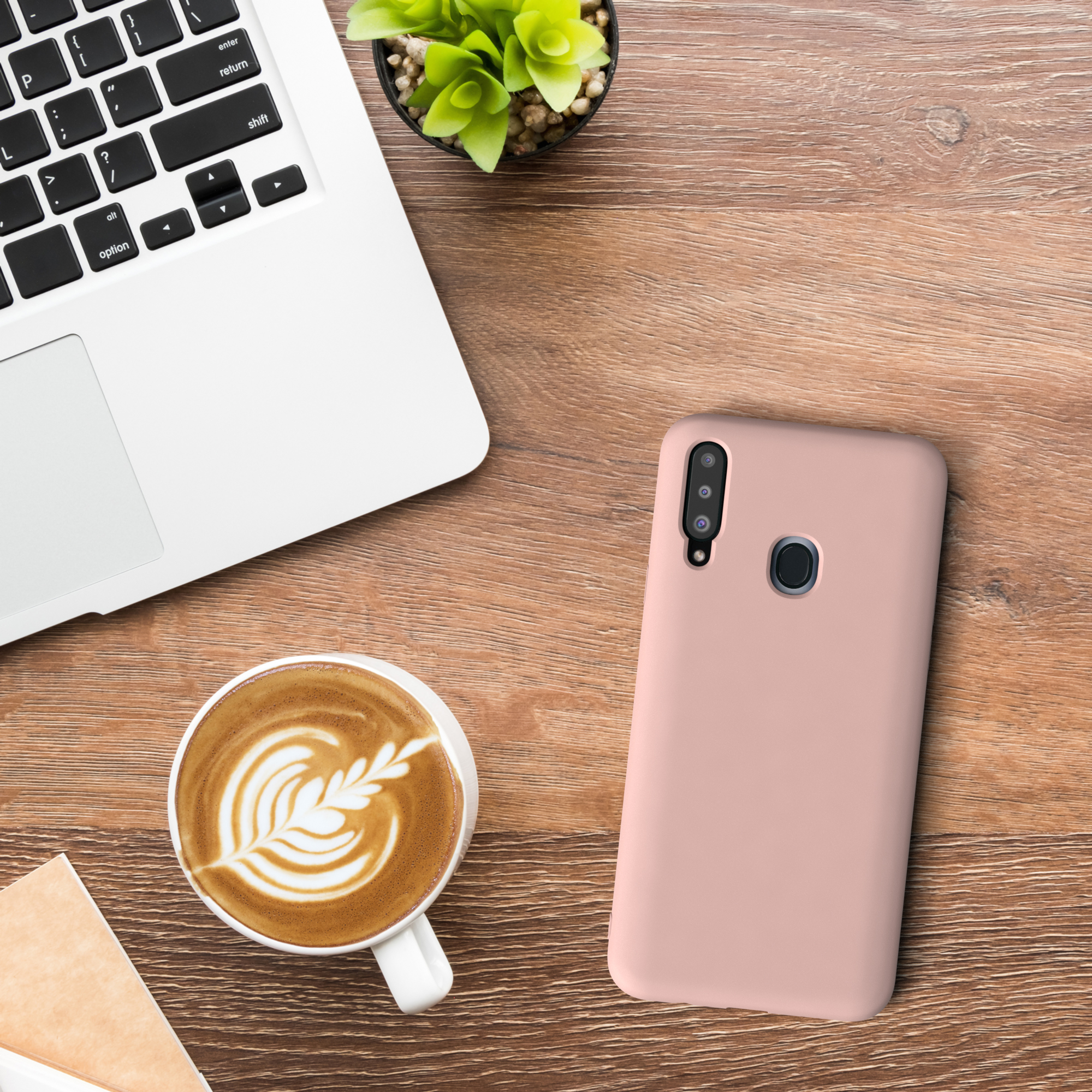 Laptop, Kaffeetasse mit Latte Art und eine pinke Handyhülle auf einem Holzschreibtisch.