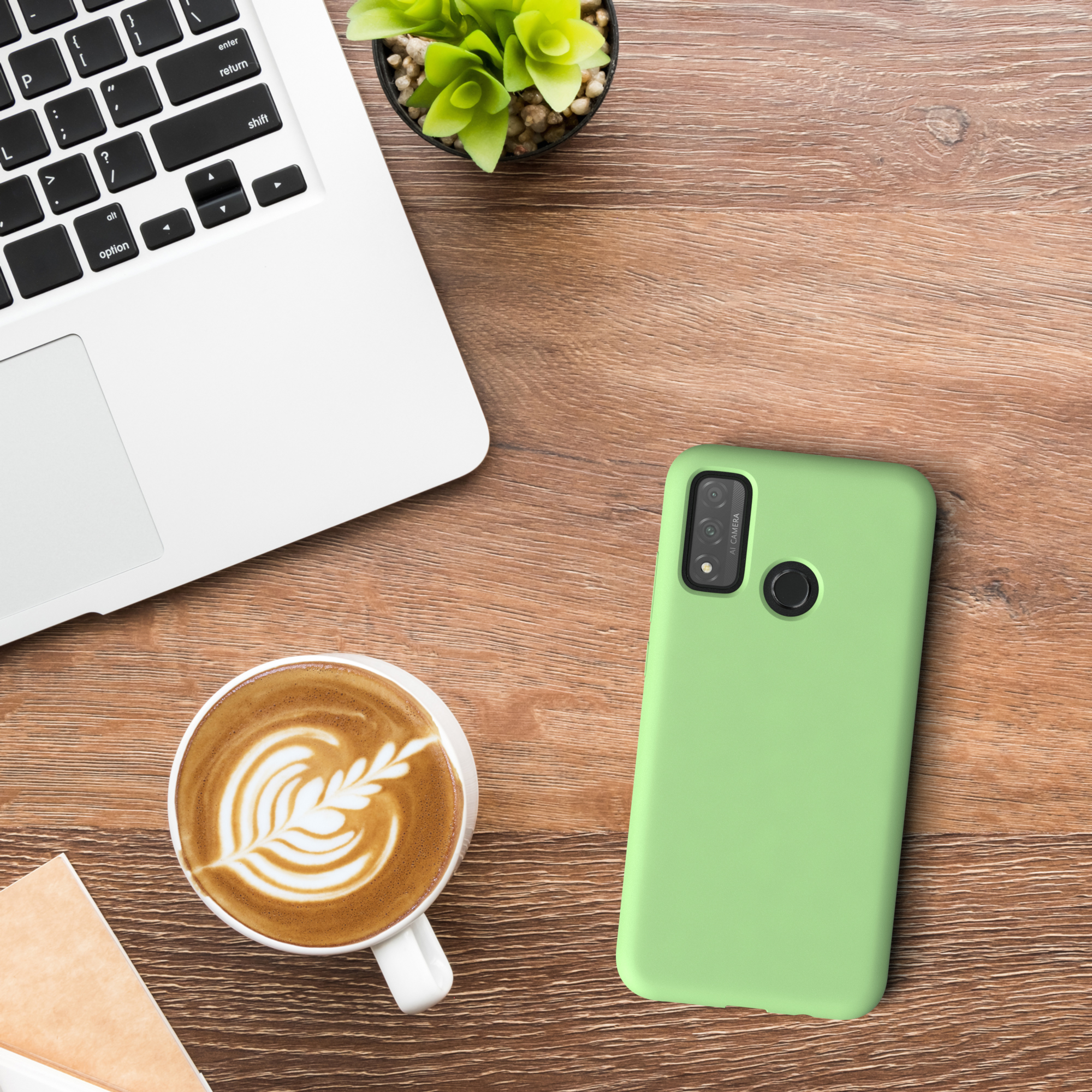 Ein Laptop, eine Kaffeetasse und eine grüne Handyhülle auf einem Holztisch. Draufsicht.